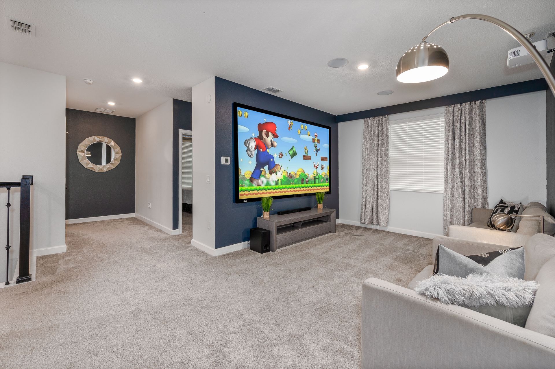 Living room with large screen displaying Mario. Gray carpet, blue accent wall, couch, and window.