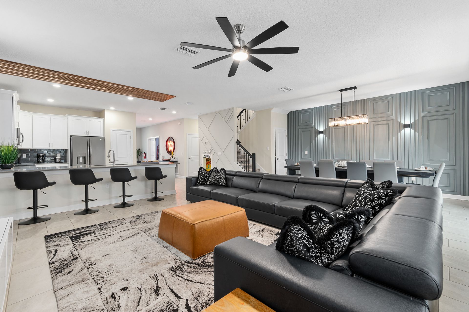 Open-concept living space with kitchen, dining area, and black leather sectional. Modern decor with neutral tones.
