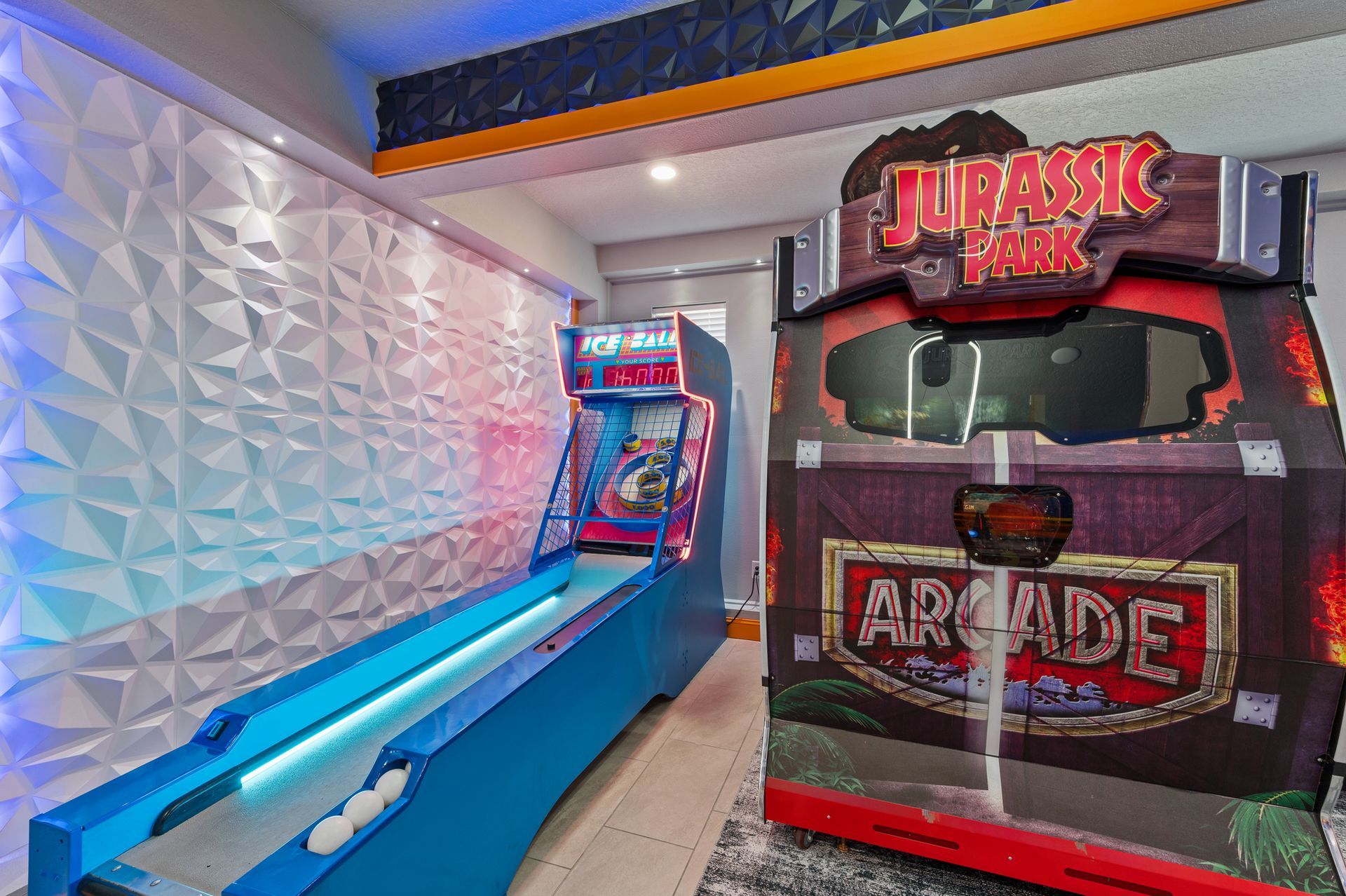 Arcade game room with a skeeball and a Jurassic Park arcade game against a textured white wall.