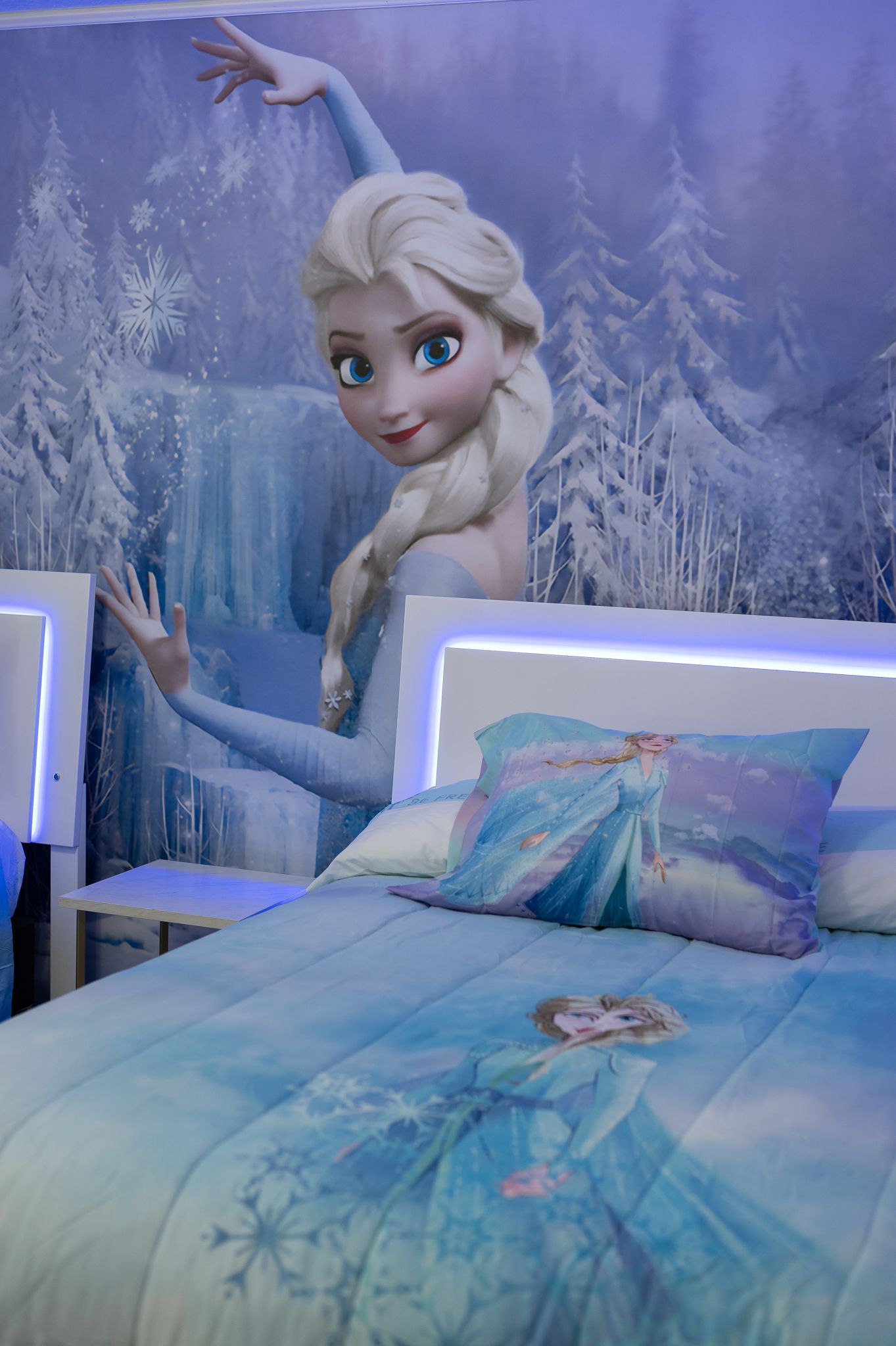 Elsa-themed bedroom with bedding and wall mural of Elsa, in blue and white.