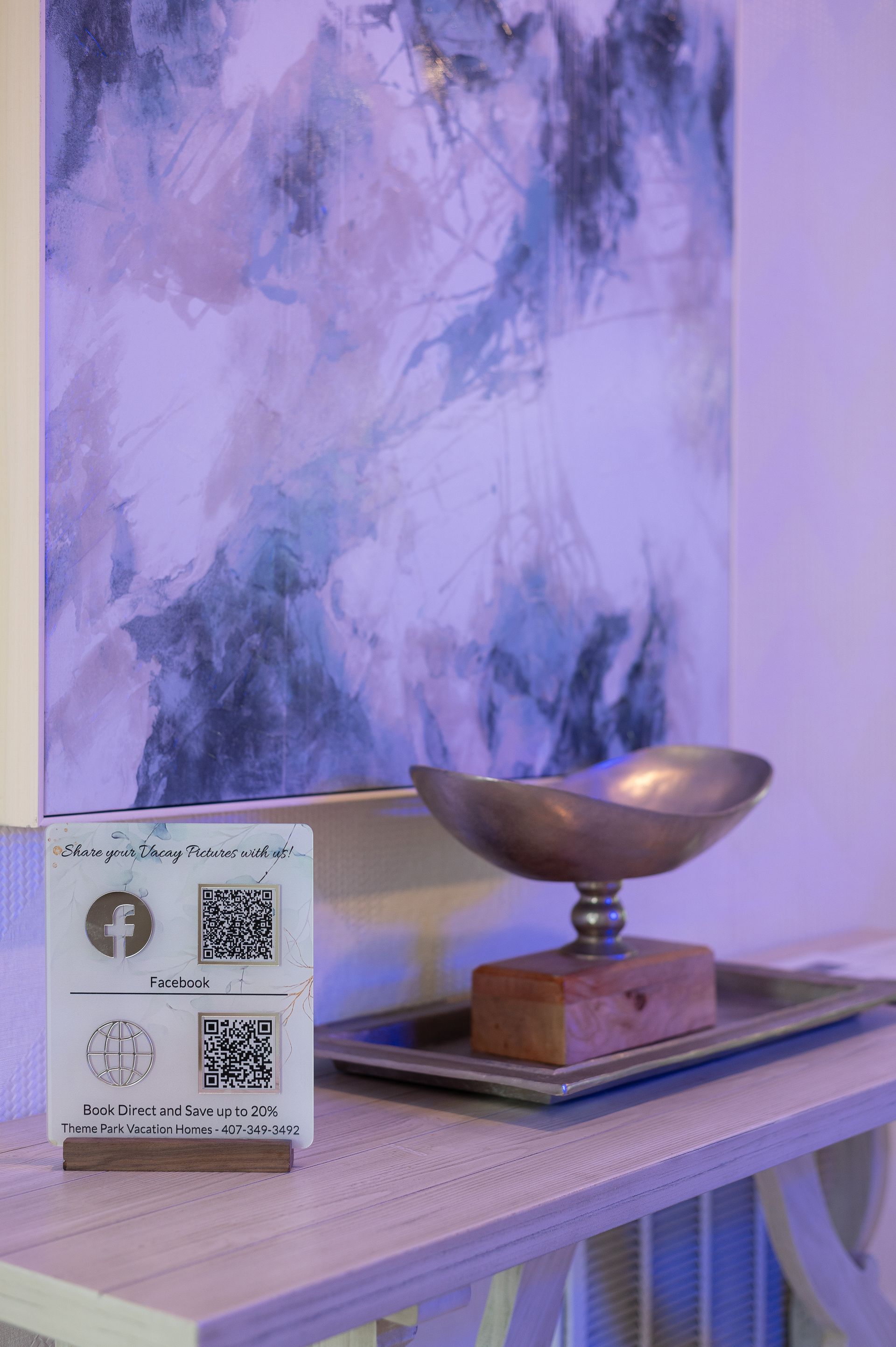 Shelf with art, QR code display, and decorative bowl. Pastel painting in background.
