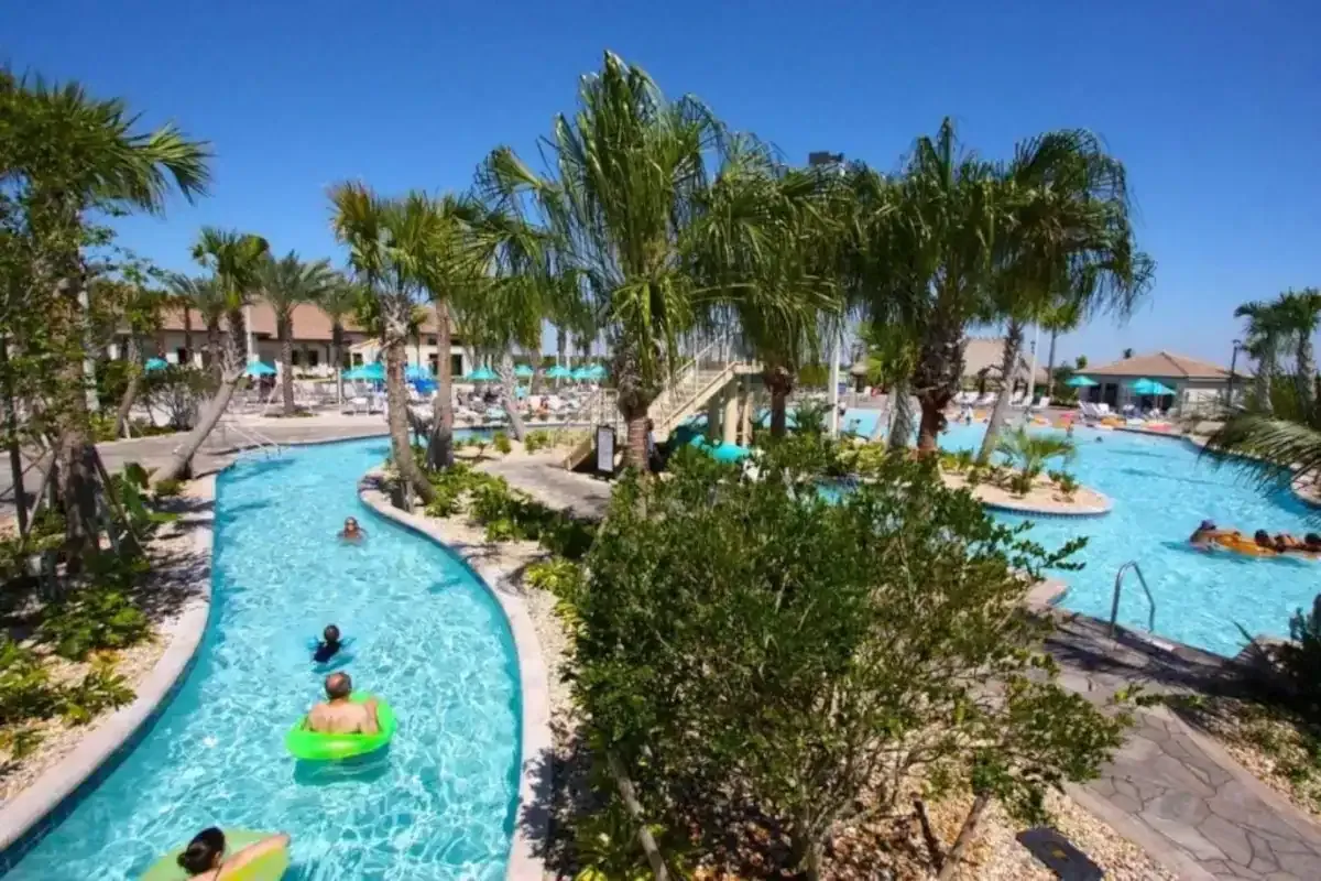 People floating in a lazy river at a tropical resort with palm trees and blue sky.