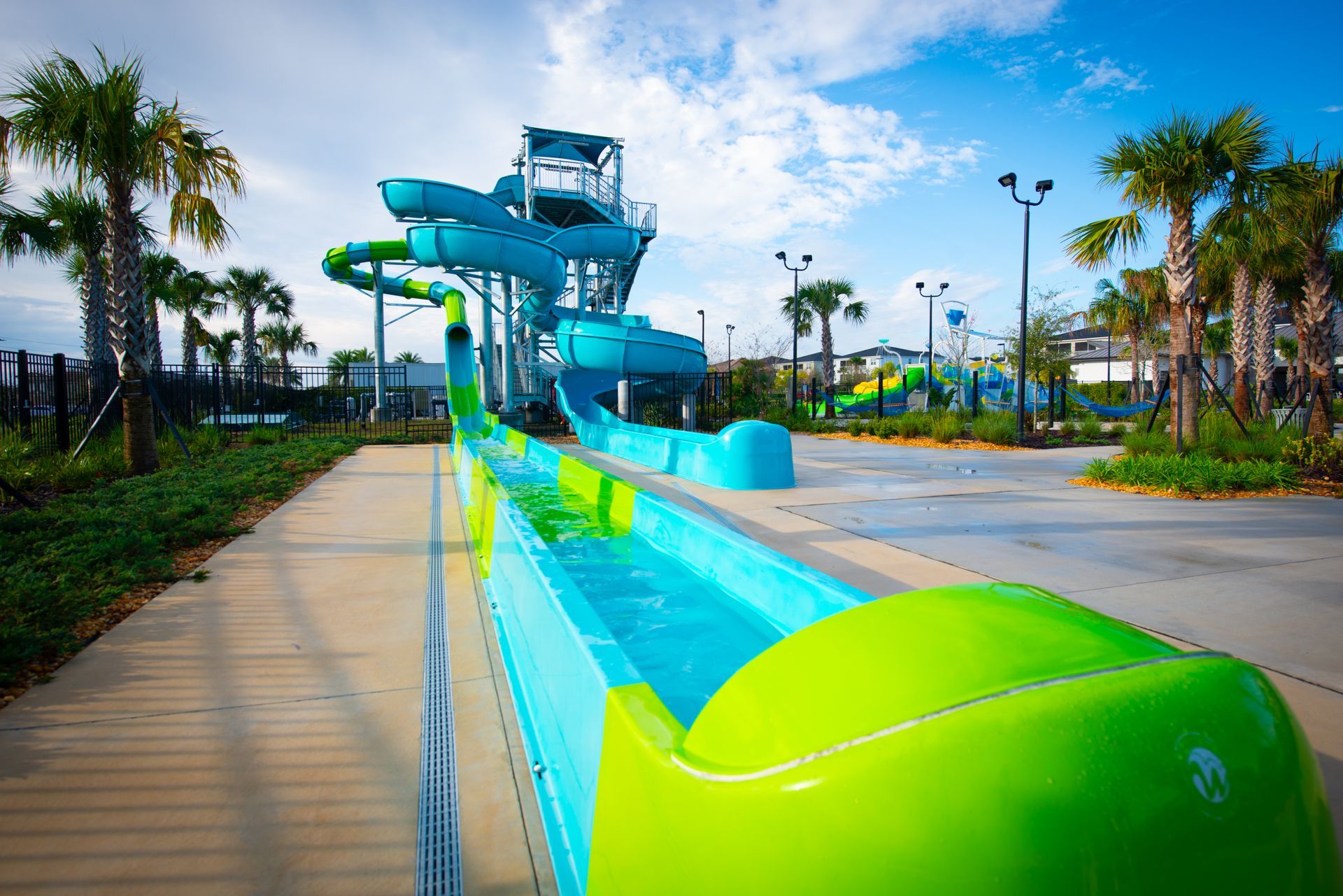 Water slide at a water park; blue and green, tall structure; palm trees in background.