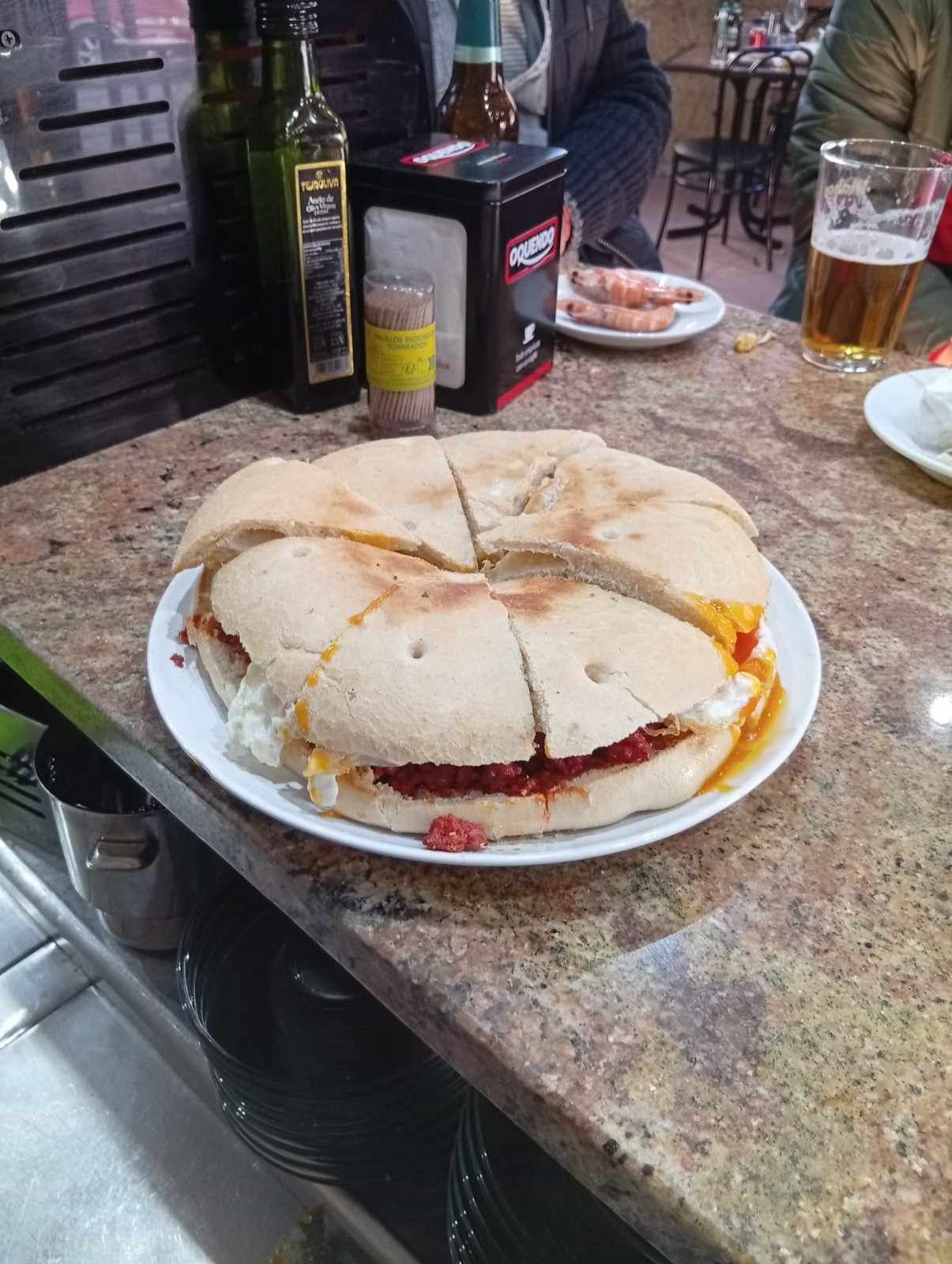 Un sándwich grande cortado en gajos en un plato en un bar.