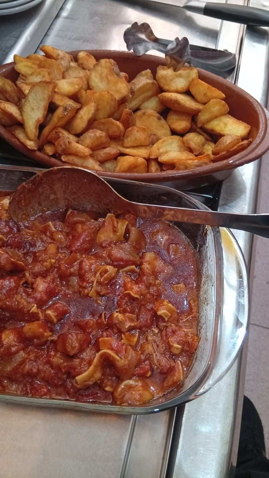 Plato de carne guisada en salsa de tomate junto a un plato de patatas gajo fritas.