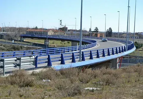Un puente azul se curva sobre un paisaje; un coche pasa por él.