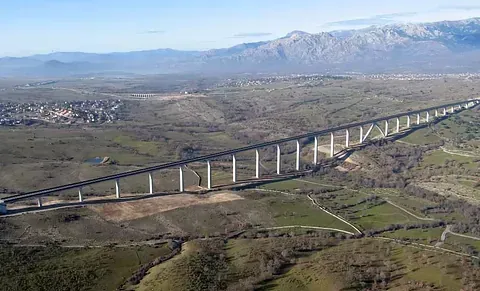 Puente de autopista elevado que cruza un valle con colinas verdes y montañas en la distancia.