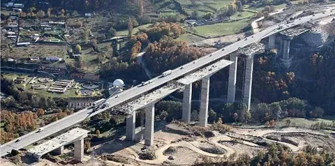 Vista aérea de un gran puente en construcción que cruza un valle, con pilares y calzadas de hormigón.