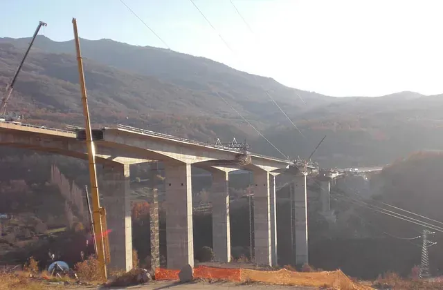 Construcción de un puente, soportes de hormigón que cruzan un valle con una montaña al fondo.