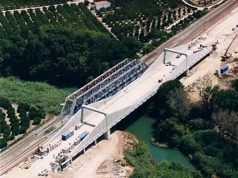Construcción de un puente sobre un río; una gran estructura metálica sostiene el puente.