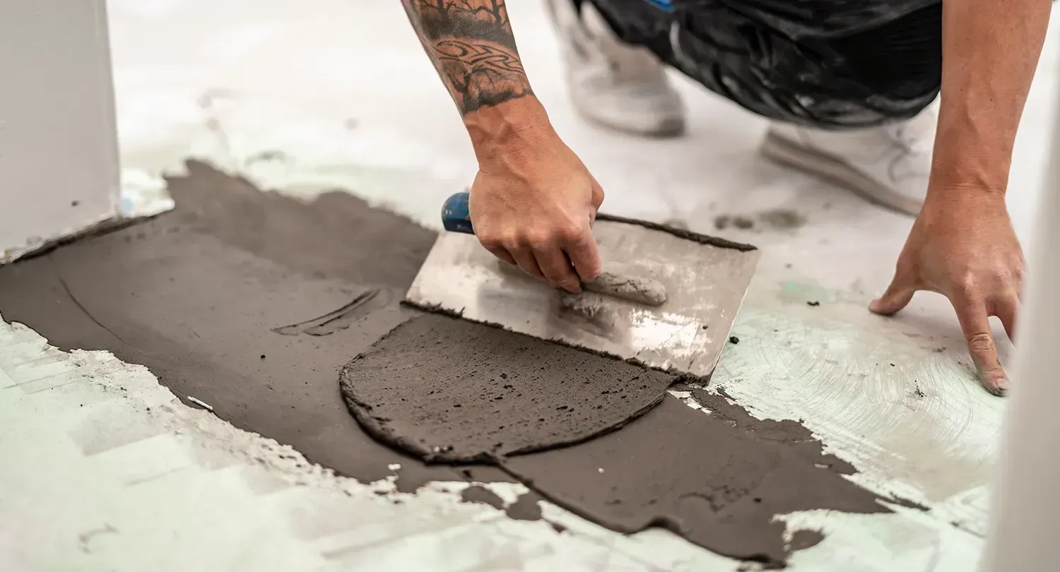 Ein Mann trägt mit einer Kelle Beton auf den Boden auf.
