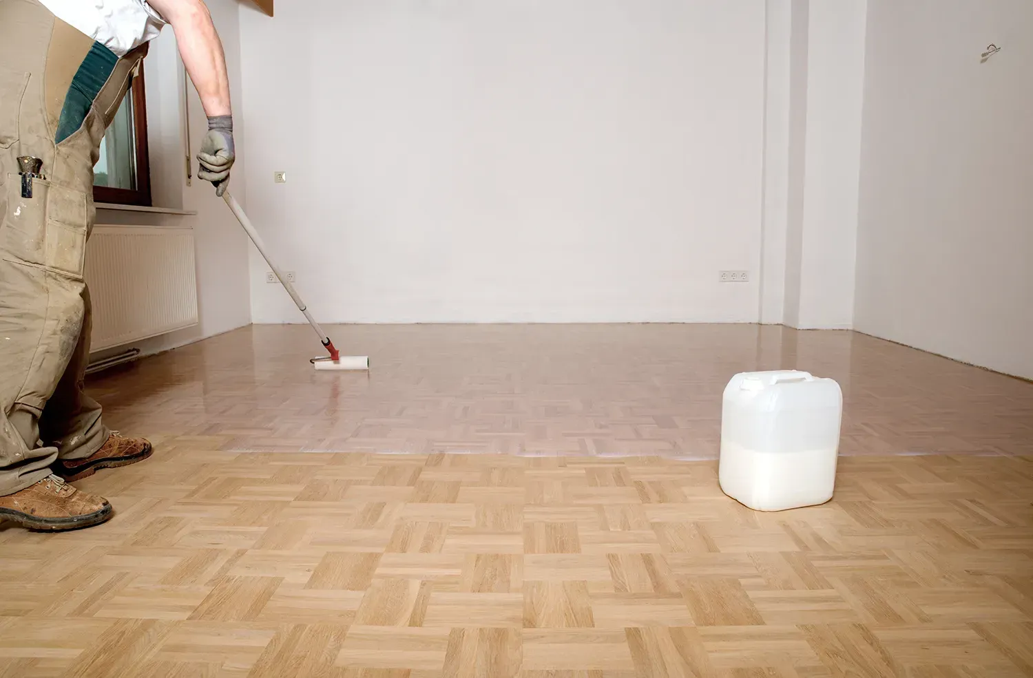 Ein Mann streicht einen Holzboden in einem leeren Raum.