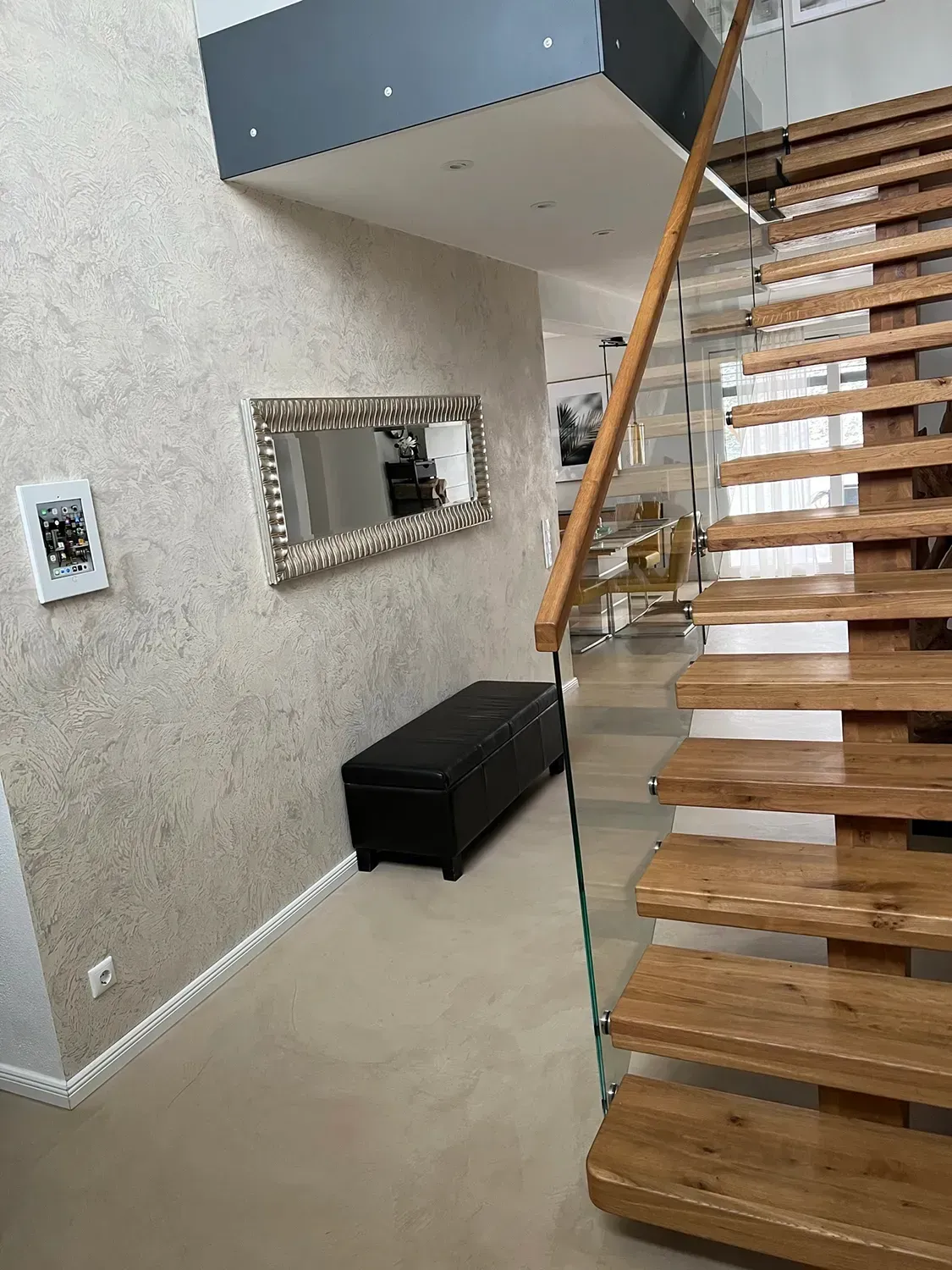 Eine Holztreppe mit einem Glasgeländer in einem Flur.