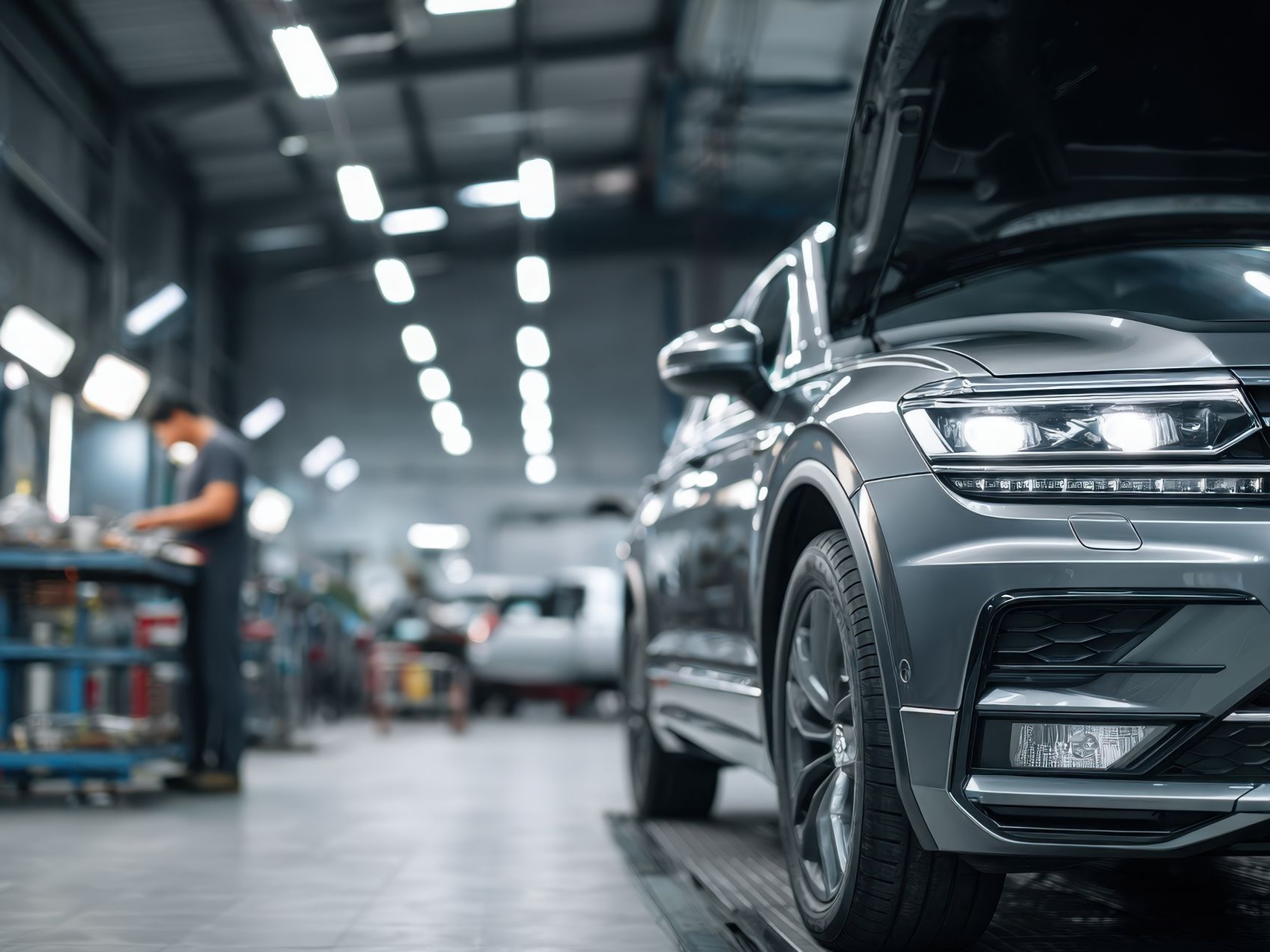 Voiture dans un atelier de réparation, capot ouvert, mécanicien au travail en arrière-plan.