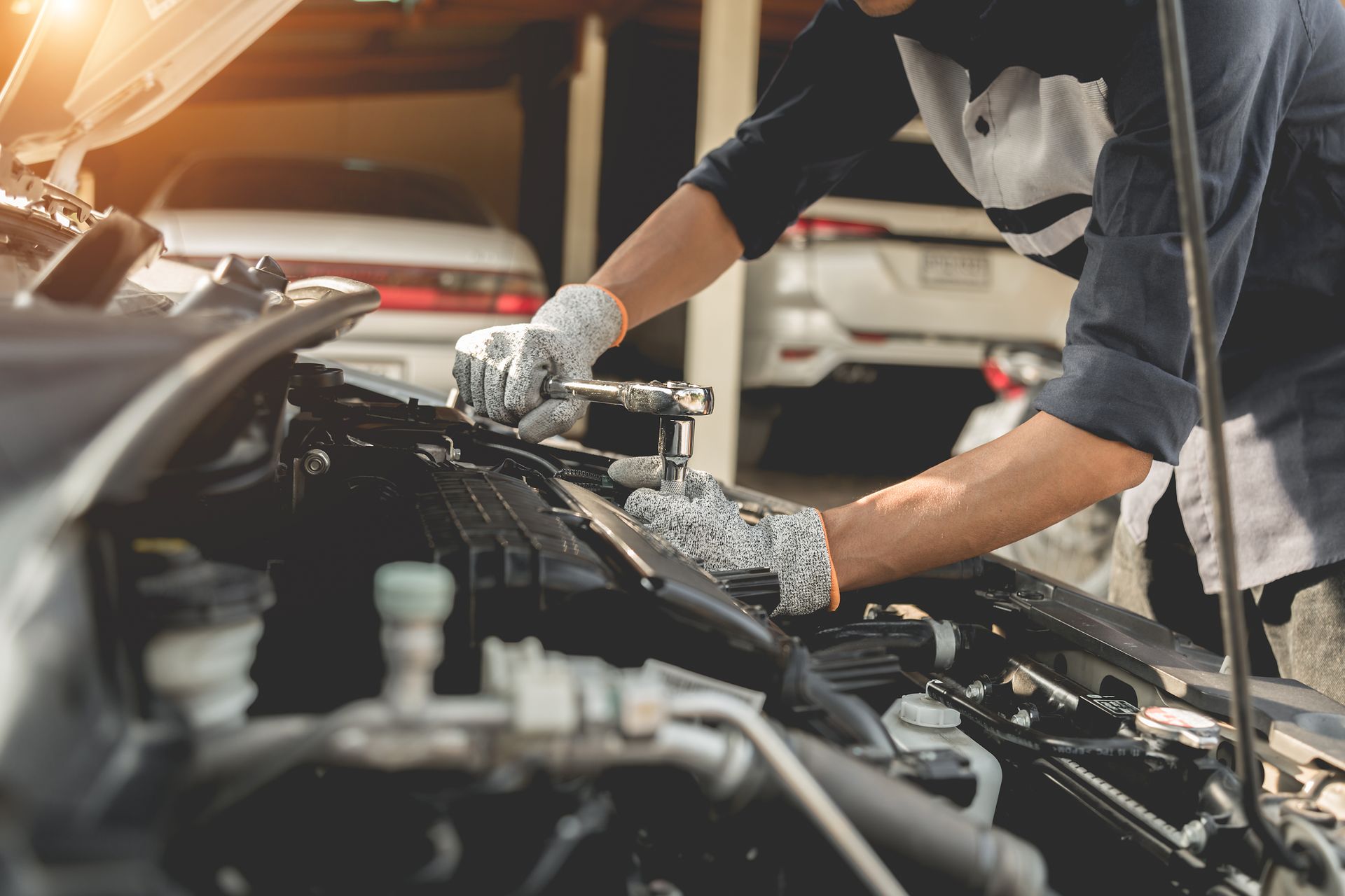 Une personne portant des gants travaille sur le compartiment moteur d'une voiture dans un garage.