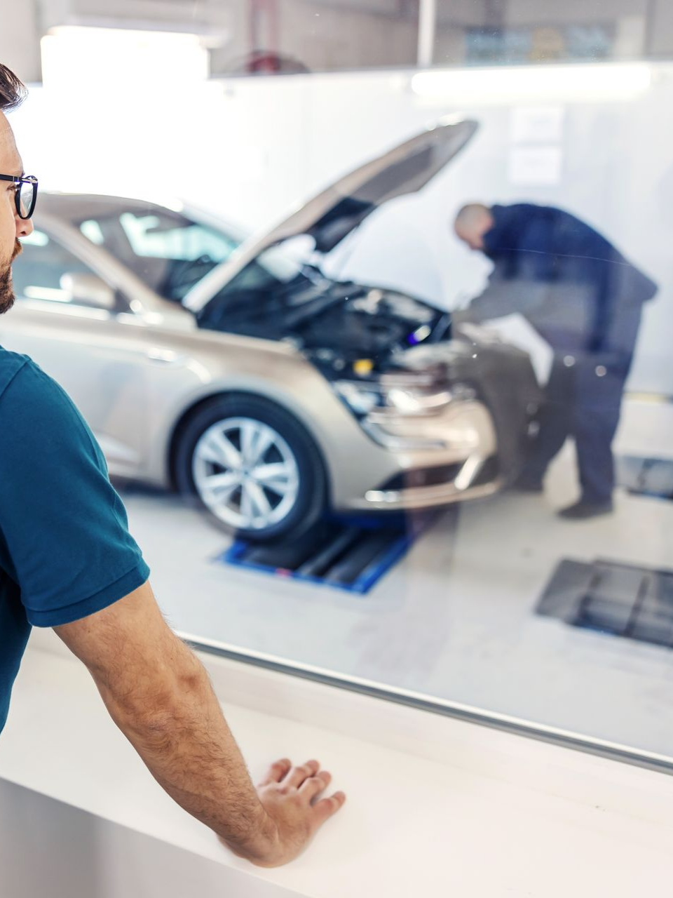Un homme observe un mécanicien travailler sur une voiture dans un atelier de réparation.