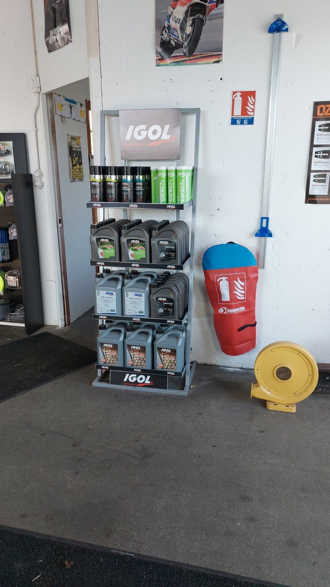 Présentoir de bouteilles et de bidons d'huile moteur sur une étagère à côté d'une poubelle rouge et d'un enrouleur jaune dans un garage