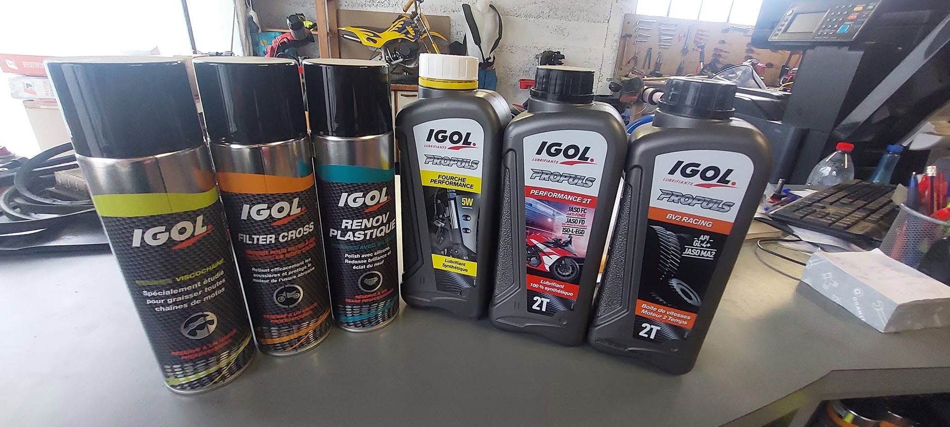 Des bidons d'huile moteur IGOL assortis, dans des emballages noirs et gris, alignés sur un établi.