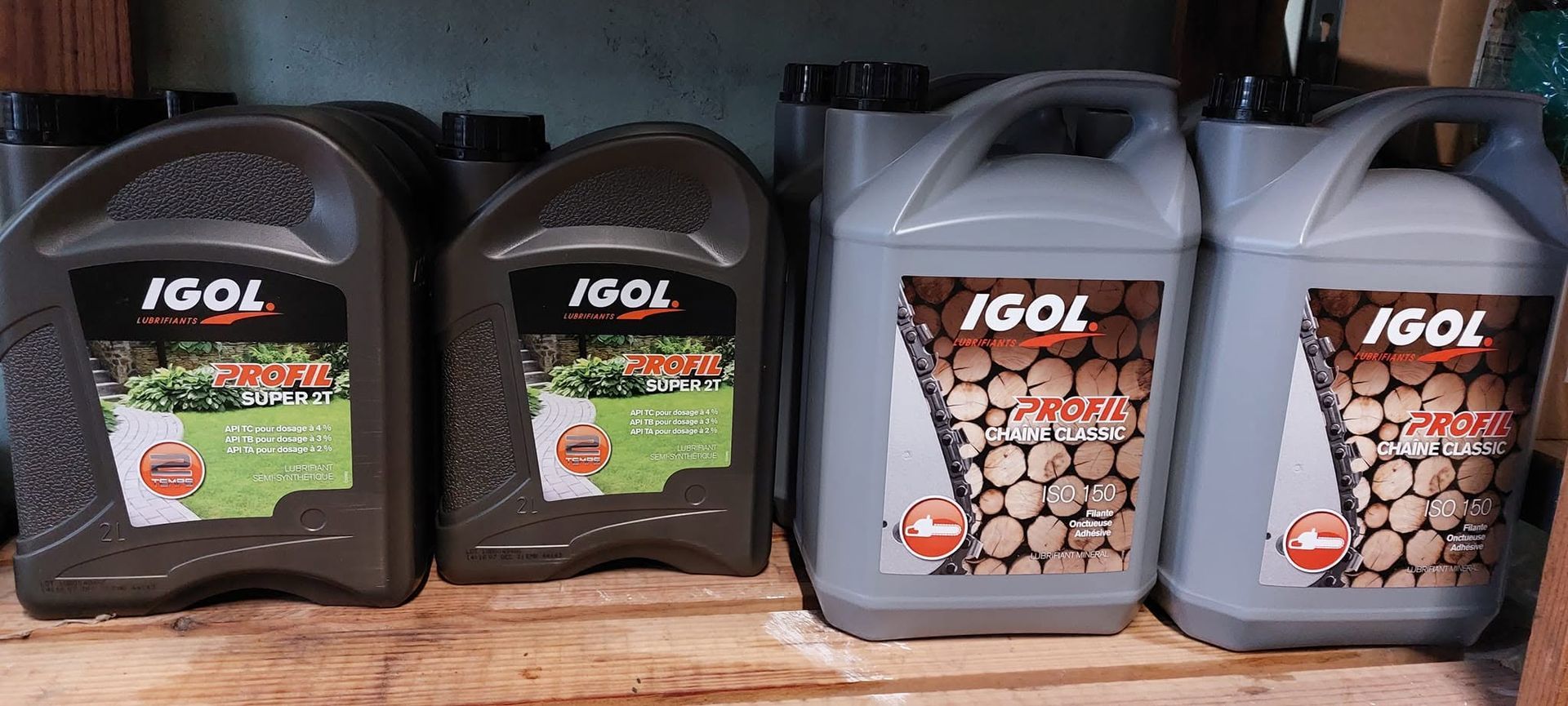 Quatre bidons de carburant IGOL noirs et gris, alignés sur une étagère en bois.