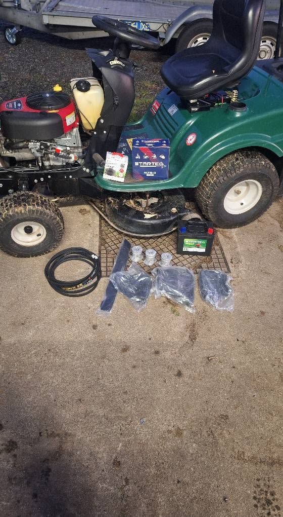 Tondeuse autoportée verte avec pièces de moteur et outils étalés sur le sol du garage