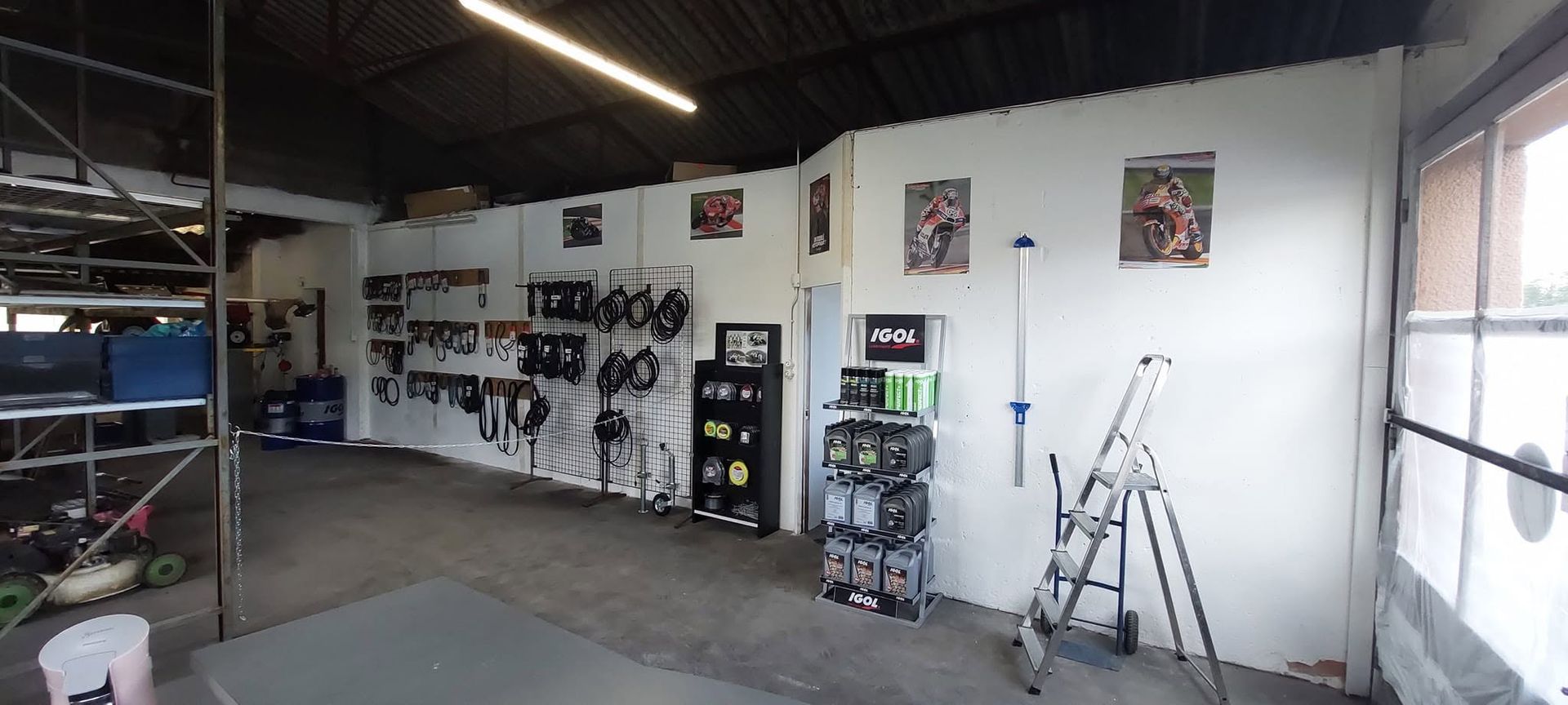 Intérieur d'atelier vide avec murs blancs, étagères, échelles et outils sous éclairage fluorescent