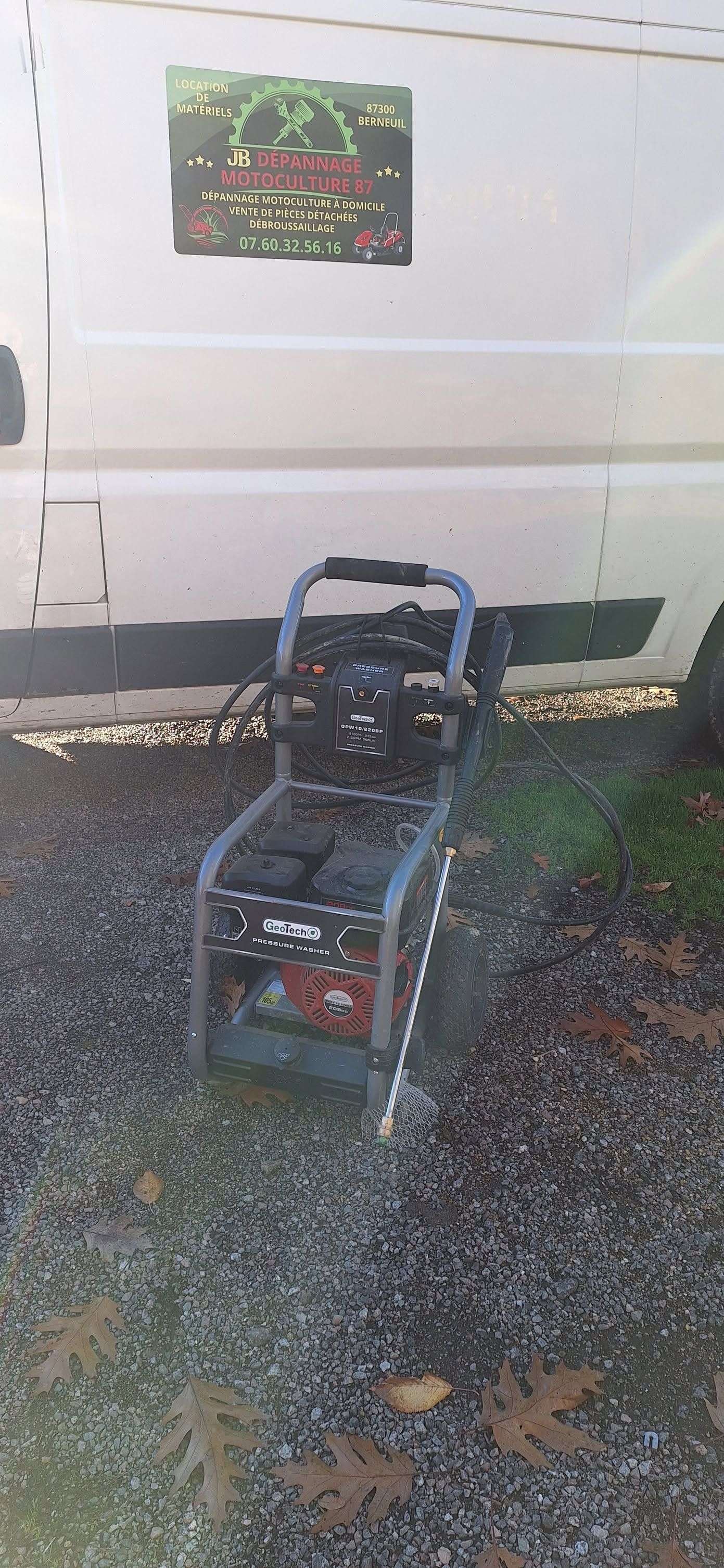 Nettoyeur haute pression portatif sur chaussée mouillée à côté d'une camionnette blanche avec une pancarte sur la porte.