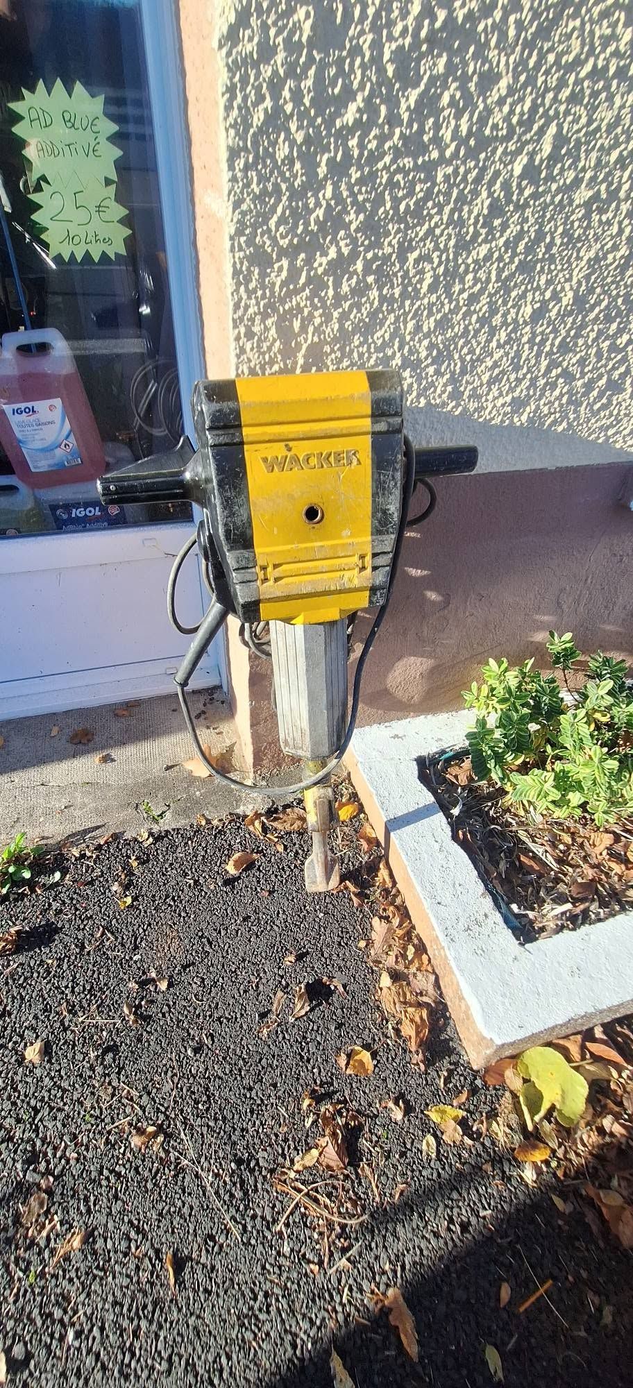 Boîte à outils jaune à côté de l'entrée d'un bâtiment et jardinière sur un sol gravillonné.