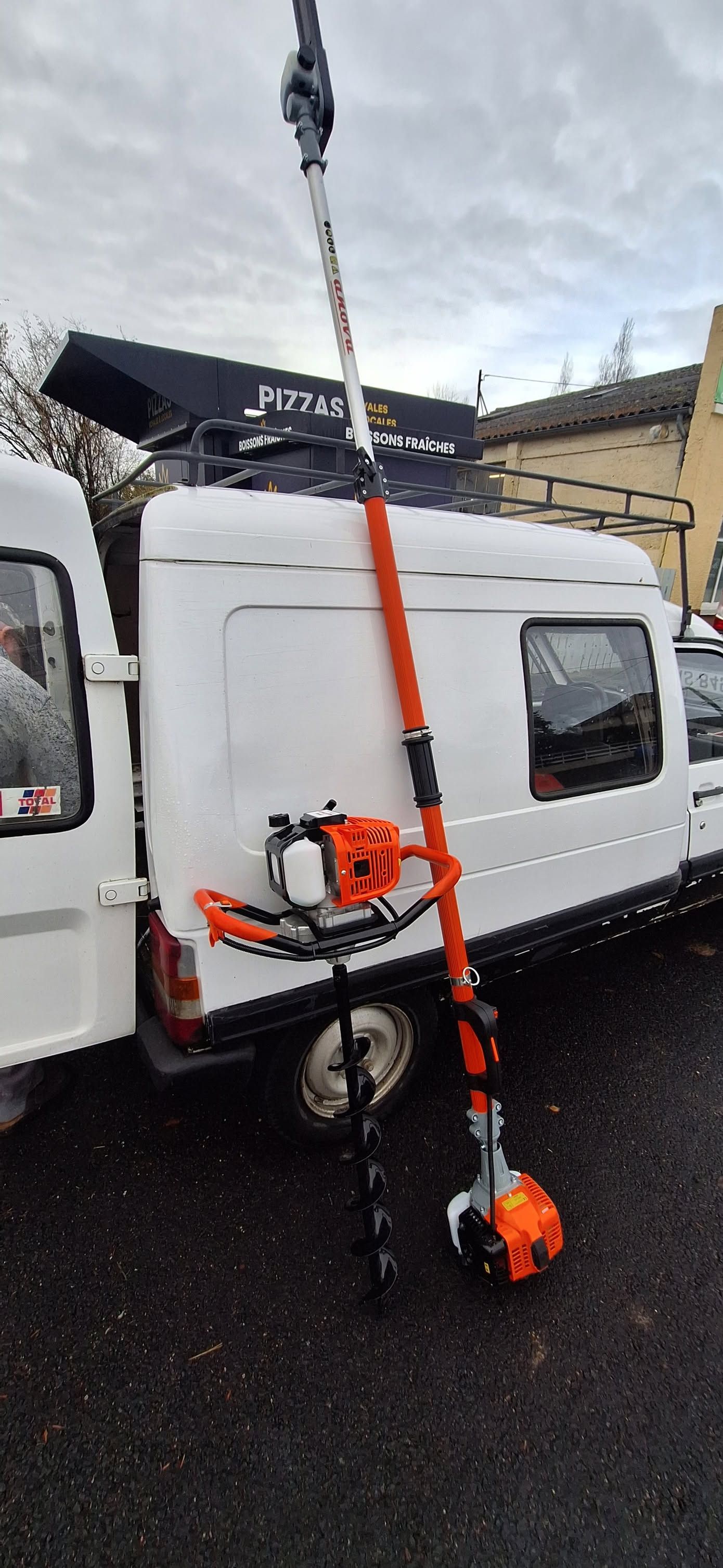 Tronçonneuse orange fixée à un grand mât sur une camionnette blanche sur un chantier