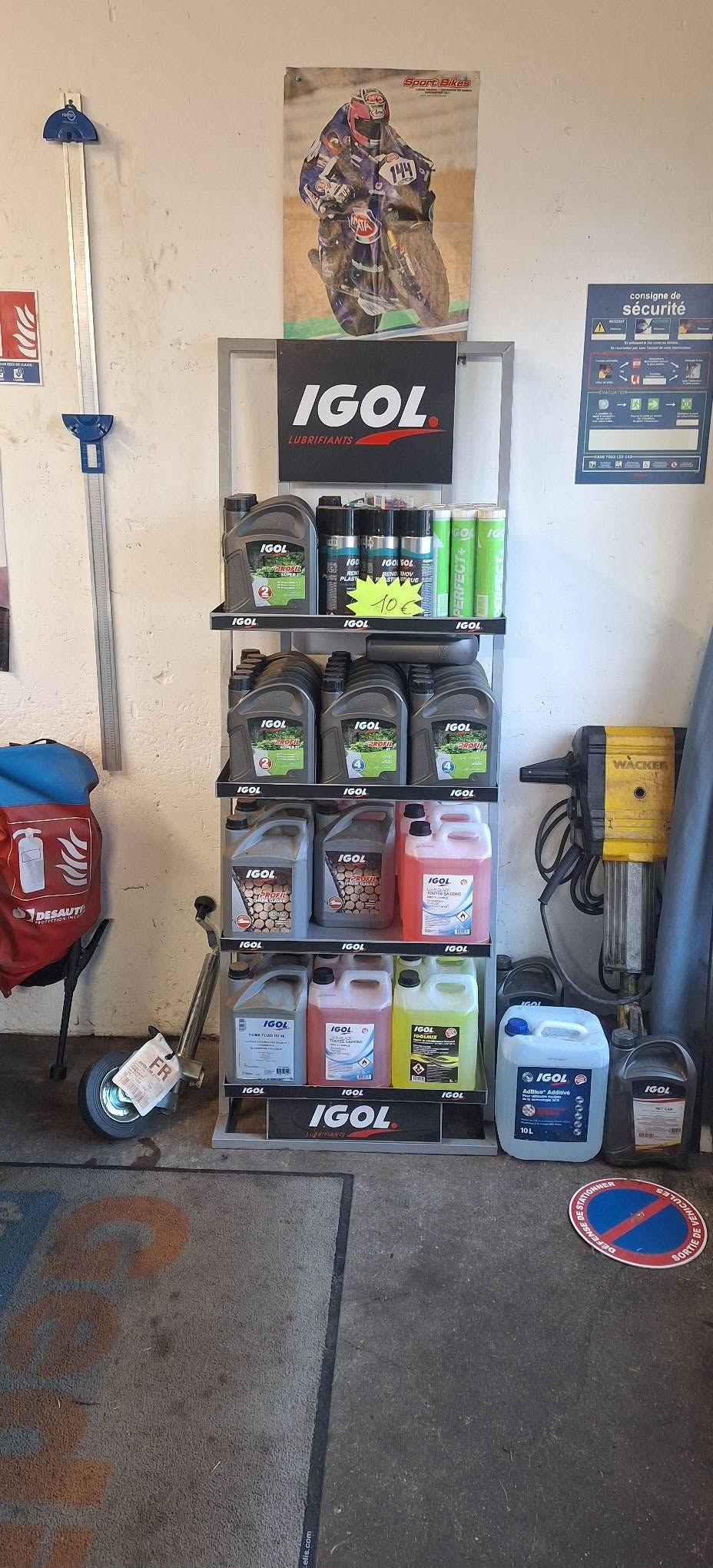 Mur de garage avec un présentoir à huile iGO, des fournitures et des outils sur un sol en béton.
