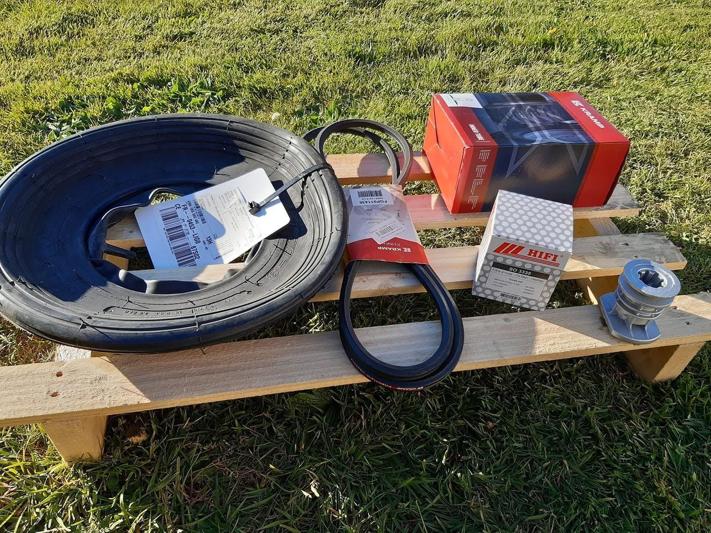 Câble enroulé, sangle, boîte à outils rouge et petites pièces de quincaillerie sur une planche de bois à l'extérieur, sur l'herbe