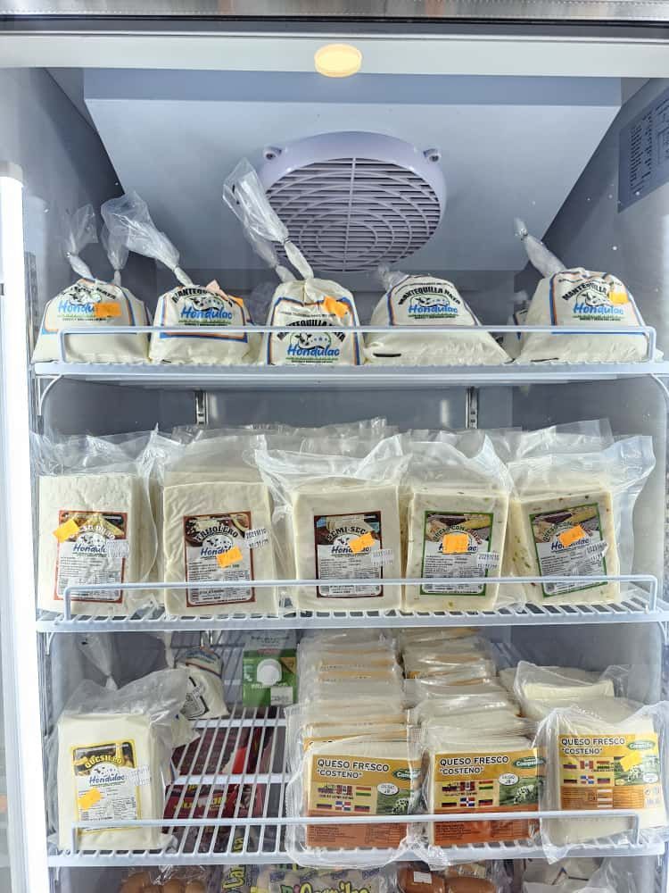 Vitrina refrigerada llena de quesos variados envasados, blancos y amarillos, con etiquetas.