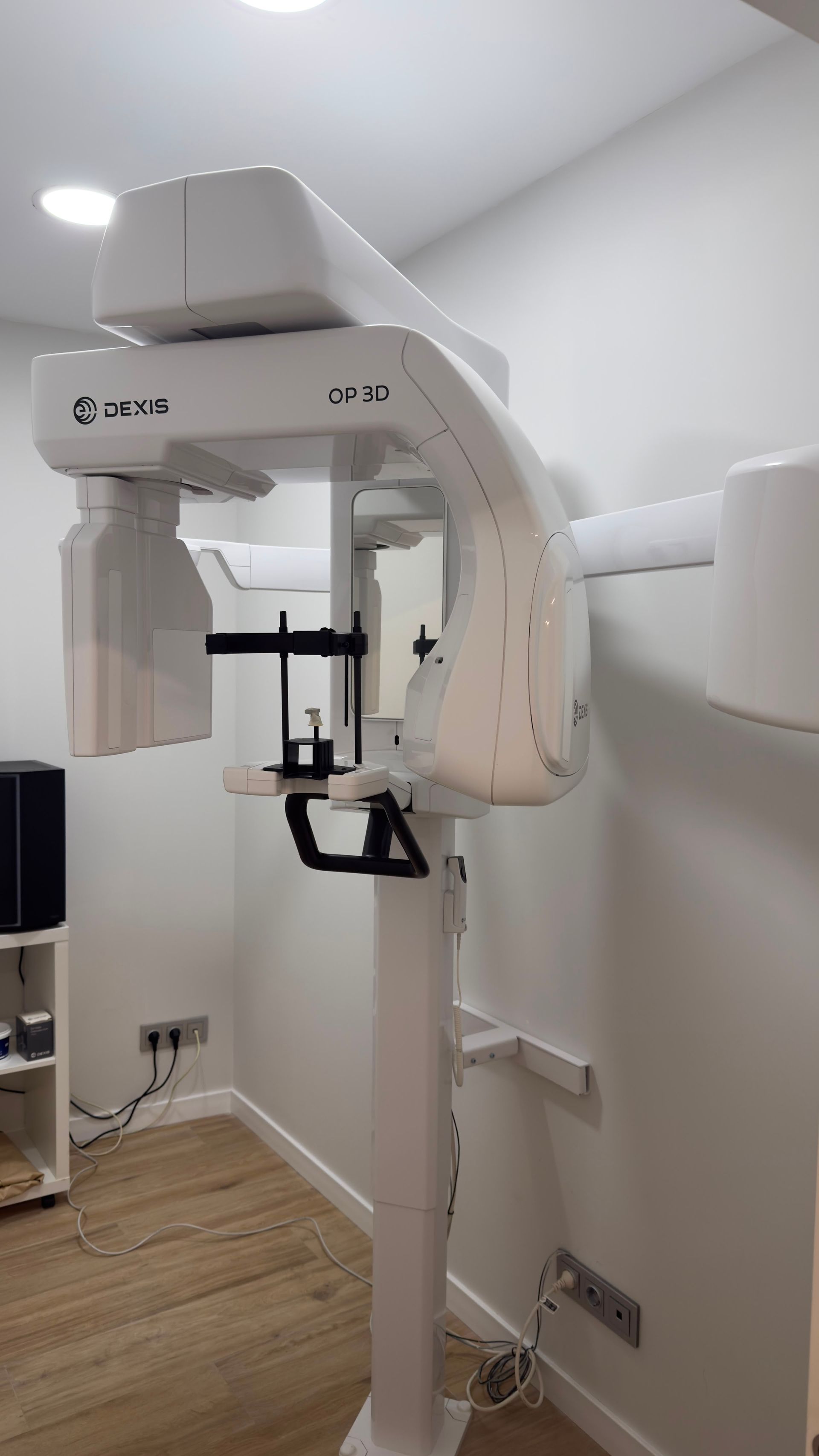 Clínica dental con sillones de tratamiento blancos, luces de techo y un monitor montado en la pared.