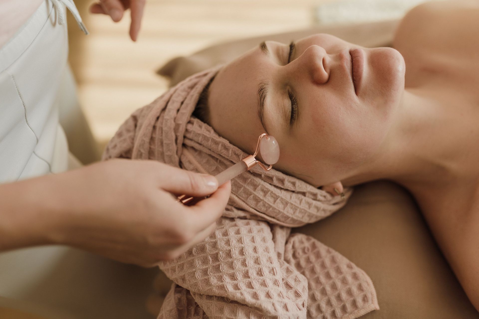 Mujer recibiendo un masaje facial mientras está tumbada en una camilla de spa, envuelta en una toalla.