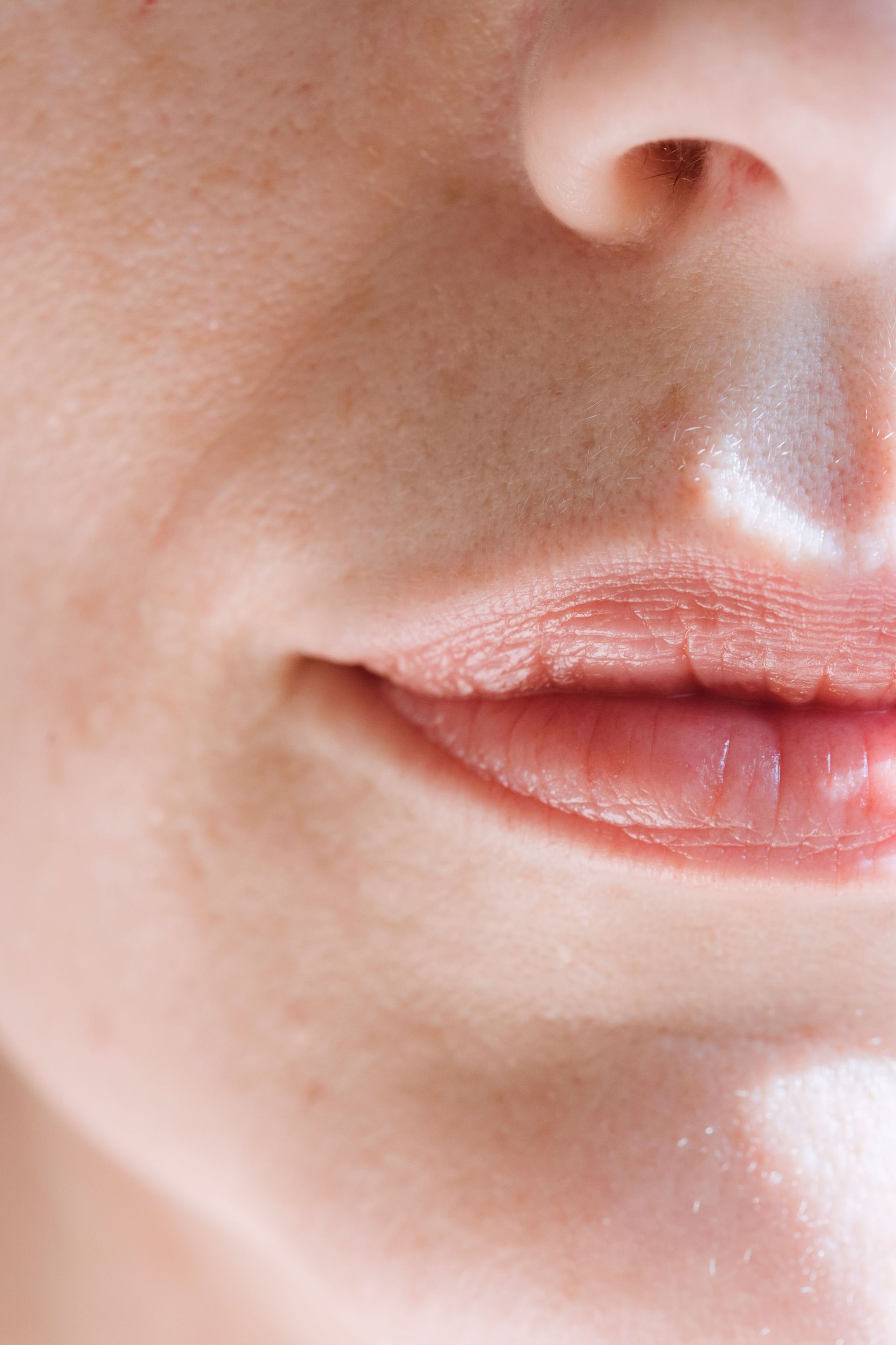 Primer plano de la nariz y los labios cerrados de una persona con un suave lápiz labial rosa.