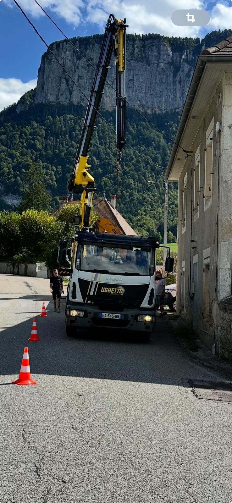 Camion avec une grue près d'un bâtiment et une montagne en arrière-plan.