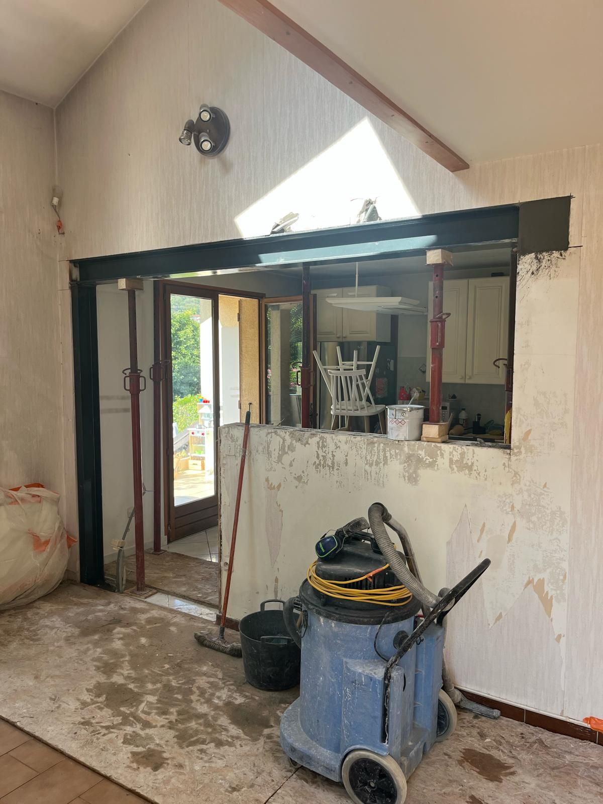 Chambre en rénovation. Murs apparents et porte ouverte. Aspirateur au premier plan.