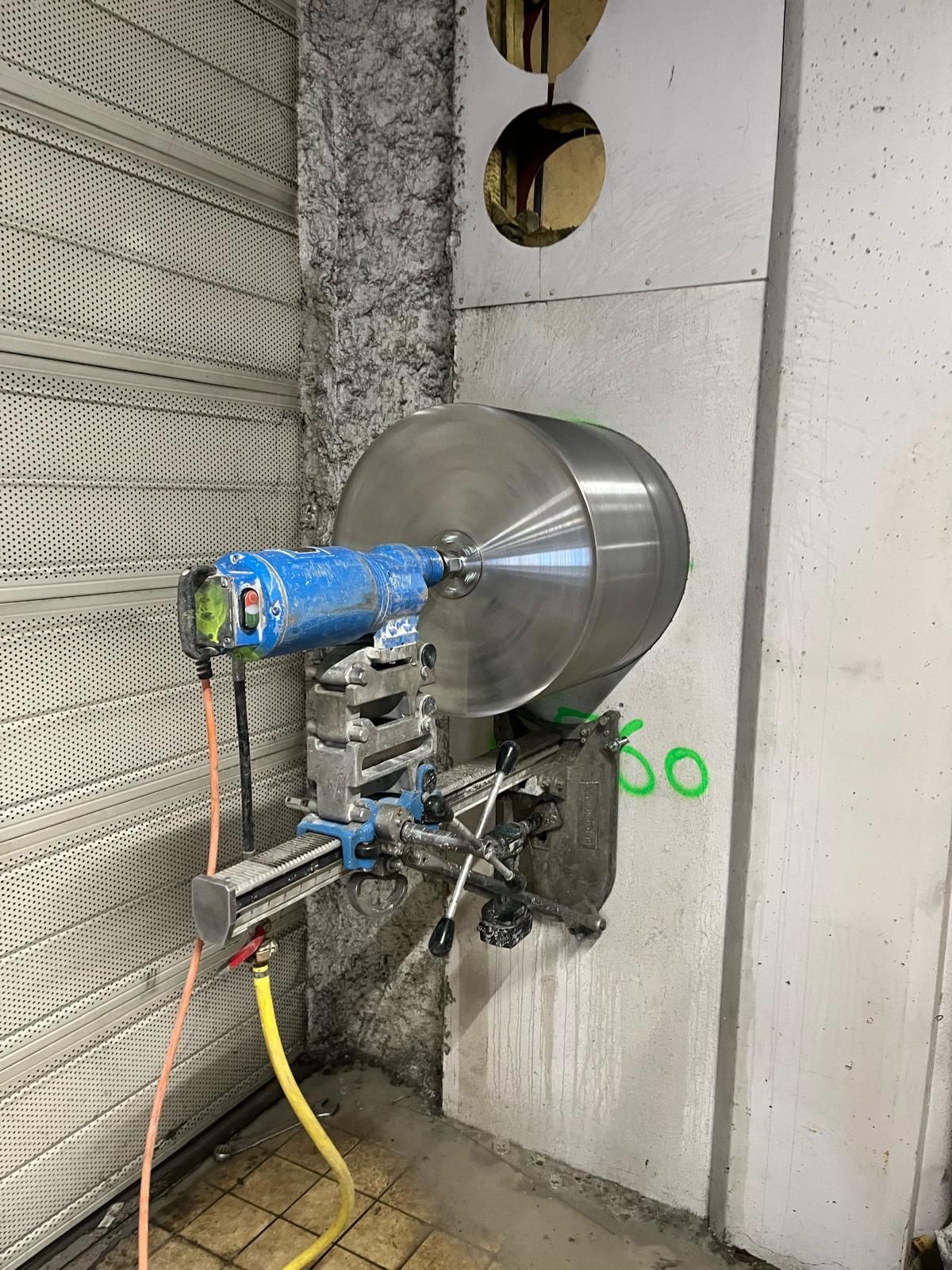 Une carotteuse à béton perce un trou dans un mur en béton. Équipement bleu, argent et jaune.
