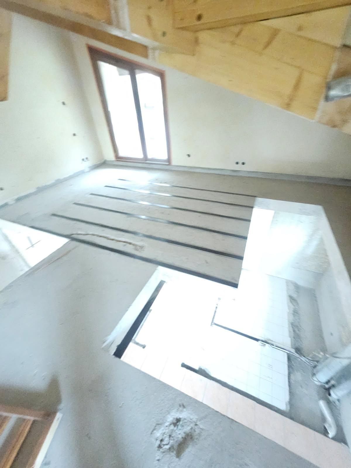 Chambre avec poutres apparentes, une fenêtre et un sol partiellement posé avec des bandes noires.