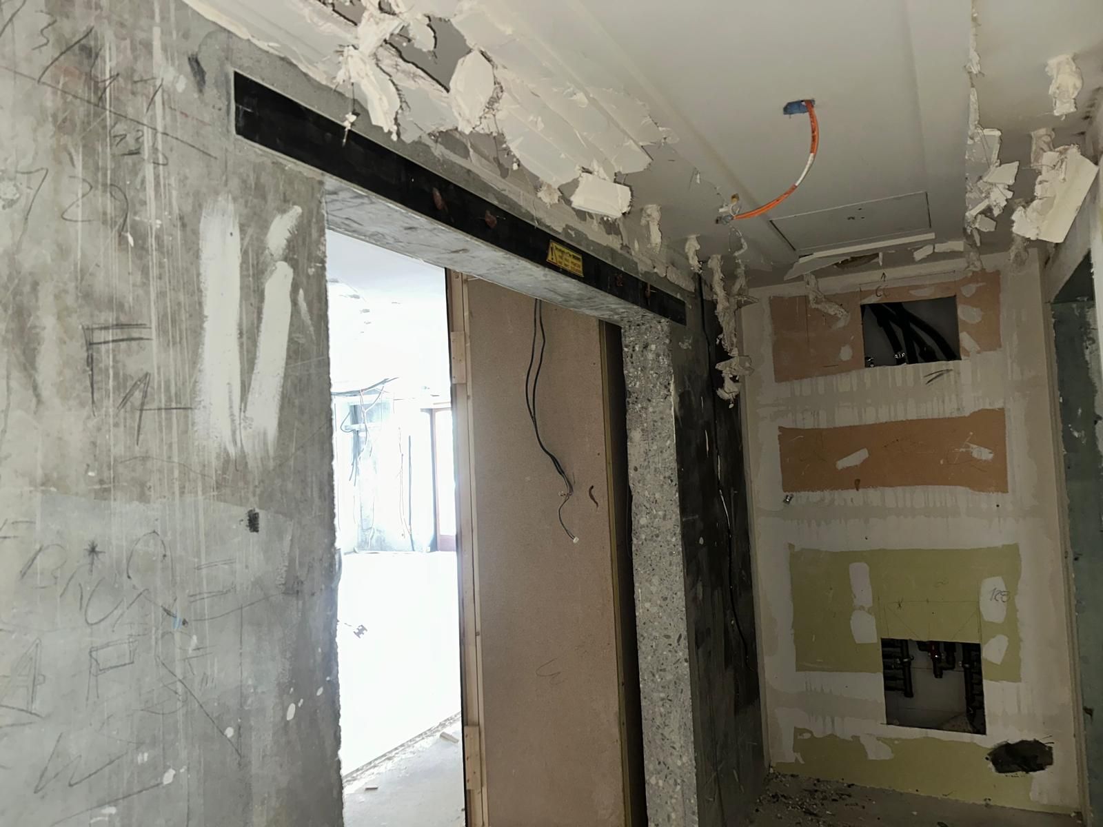 Chantier : porte avec poutre noire, câblage apparent, murs non finis.