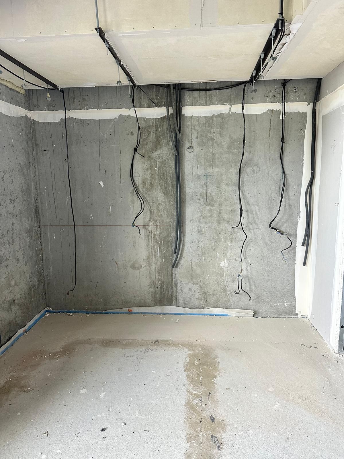 Chantier intérieur avec murs en béton, câblage électrique apparent et sol en béton.