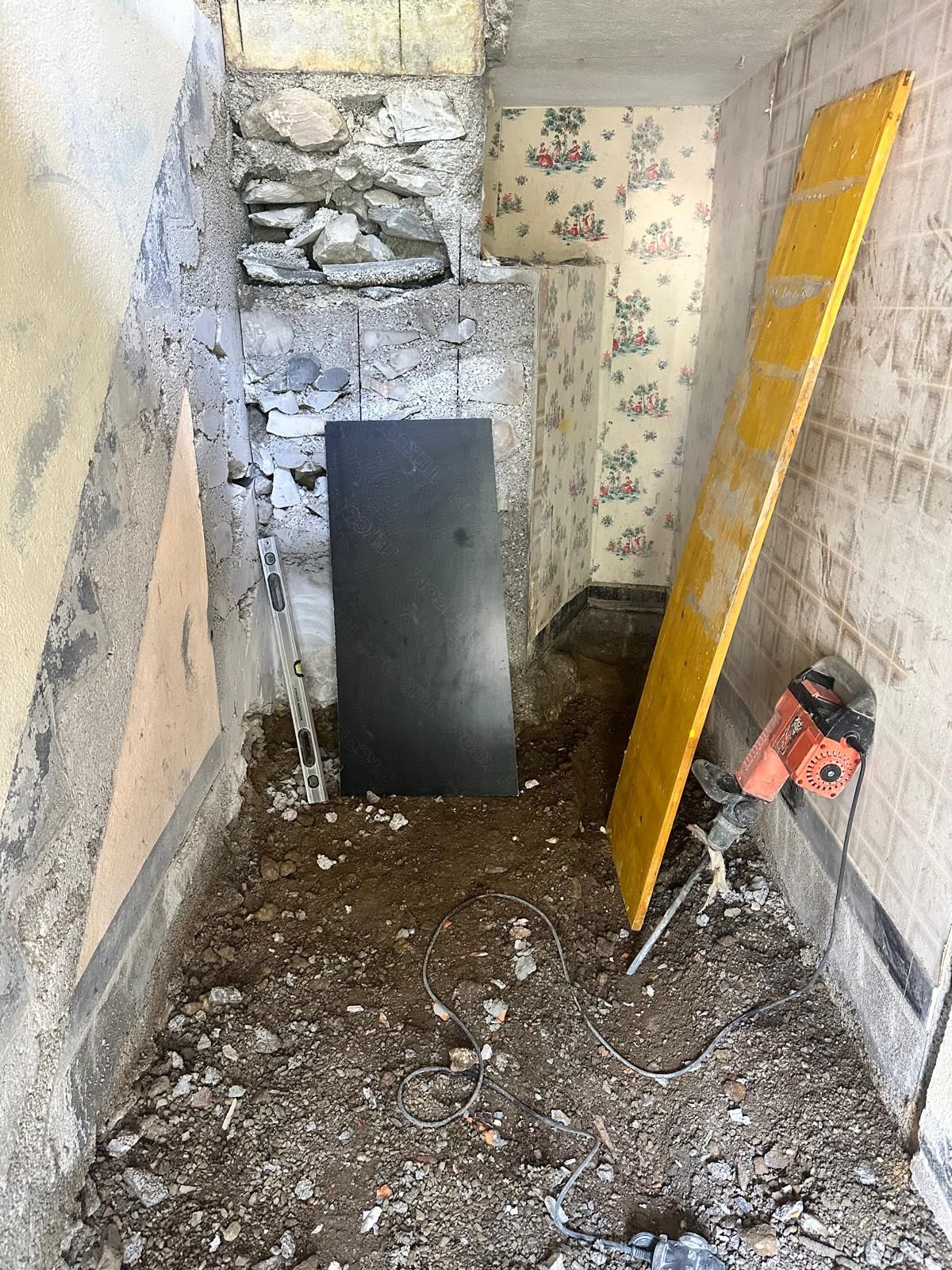 Construction dans un espace étroit et faiblement éclairé : gravats, outils et mur en pierre apparente.