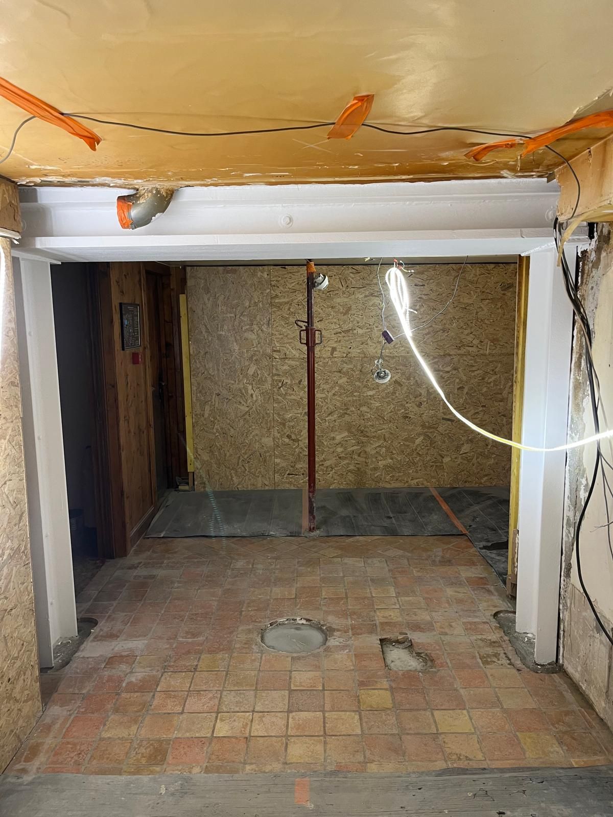 Vue intérieure d'une pièce en rénovation : sol en briques apparentes, murs bruts et porte ouverte.