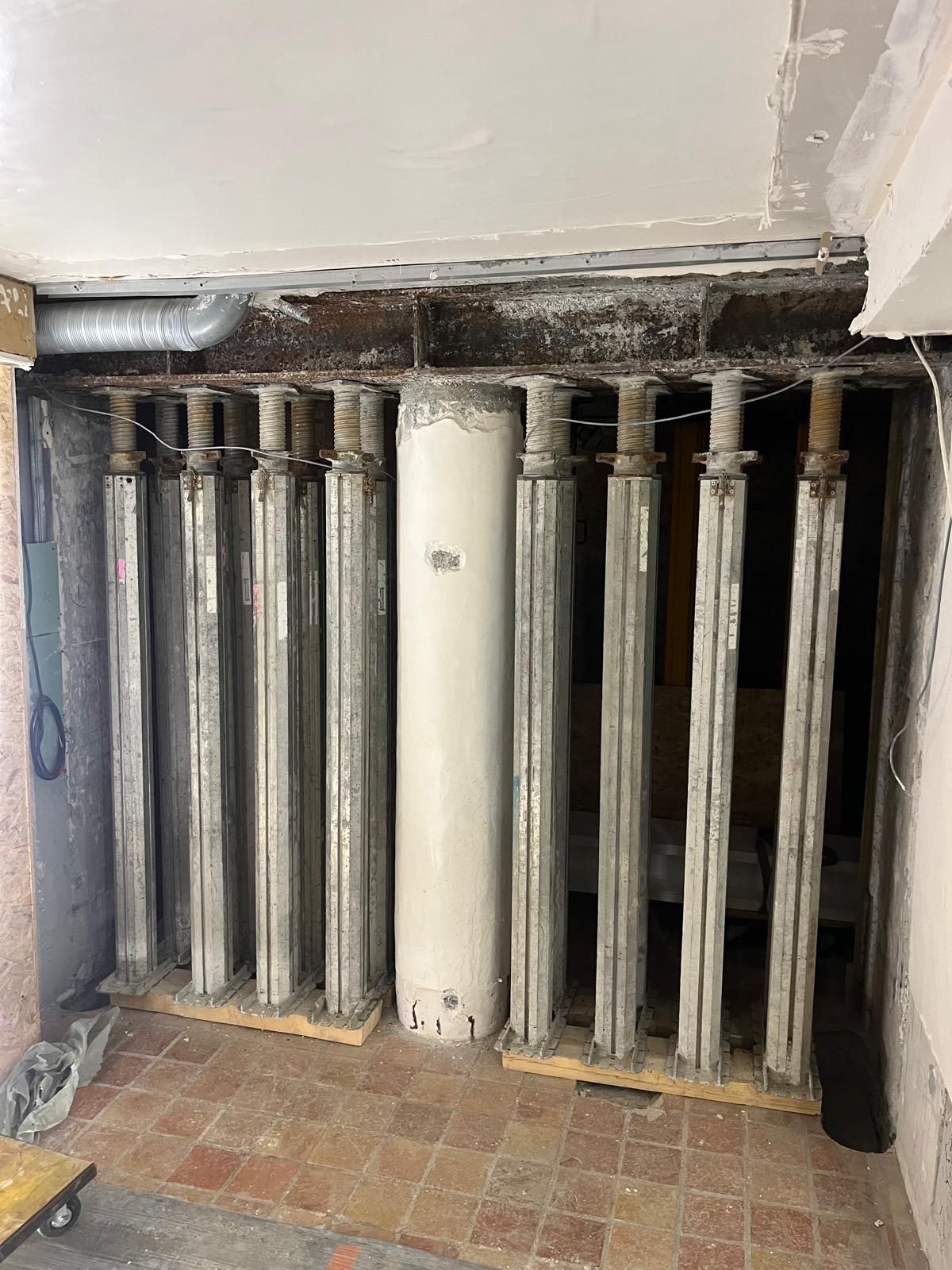 Des rangées de colonnes de support métalliques soutiennent un plafond ; un cylindre blanc se trouve au milieu.