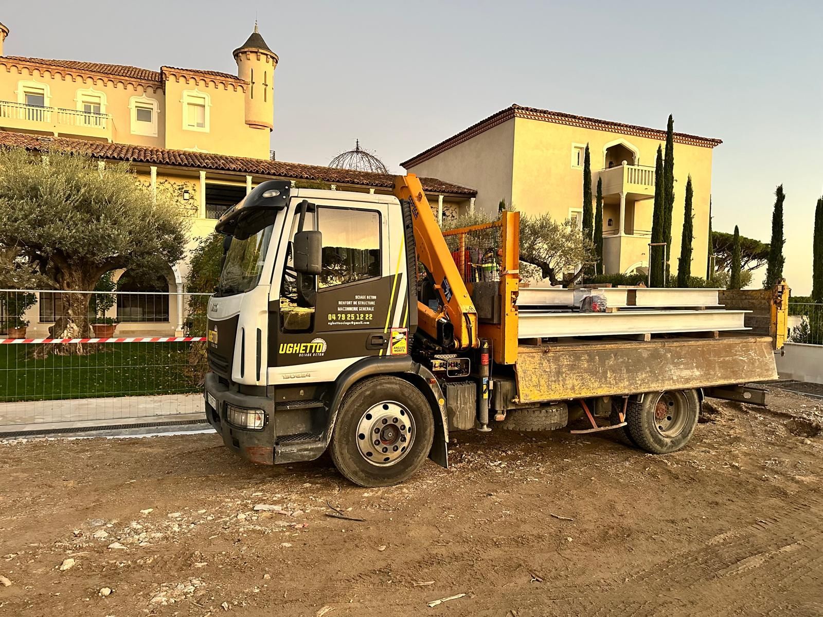Un homme portant des gants broie des blocs de béton avec une meuleuse électrique à l'extérieur, portant une chemise à carreaux et une casquette.