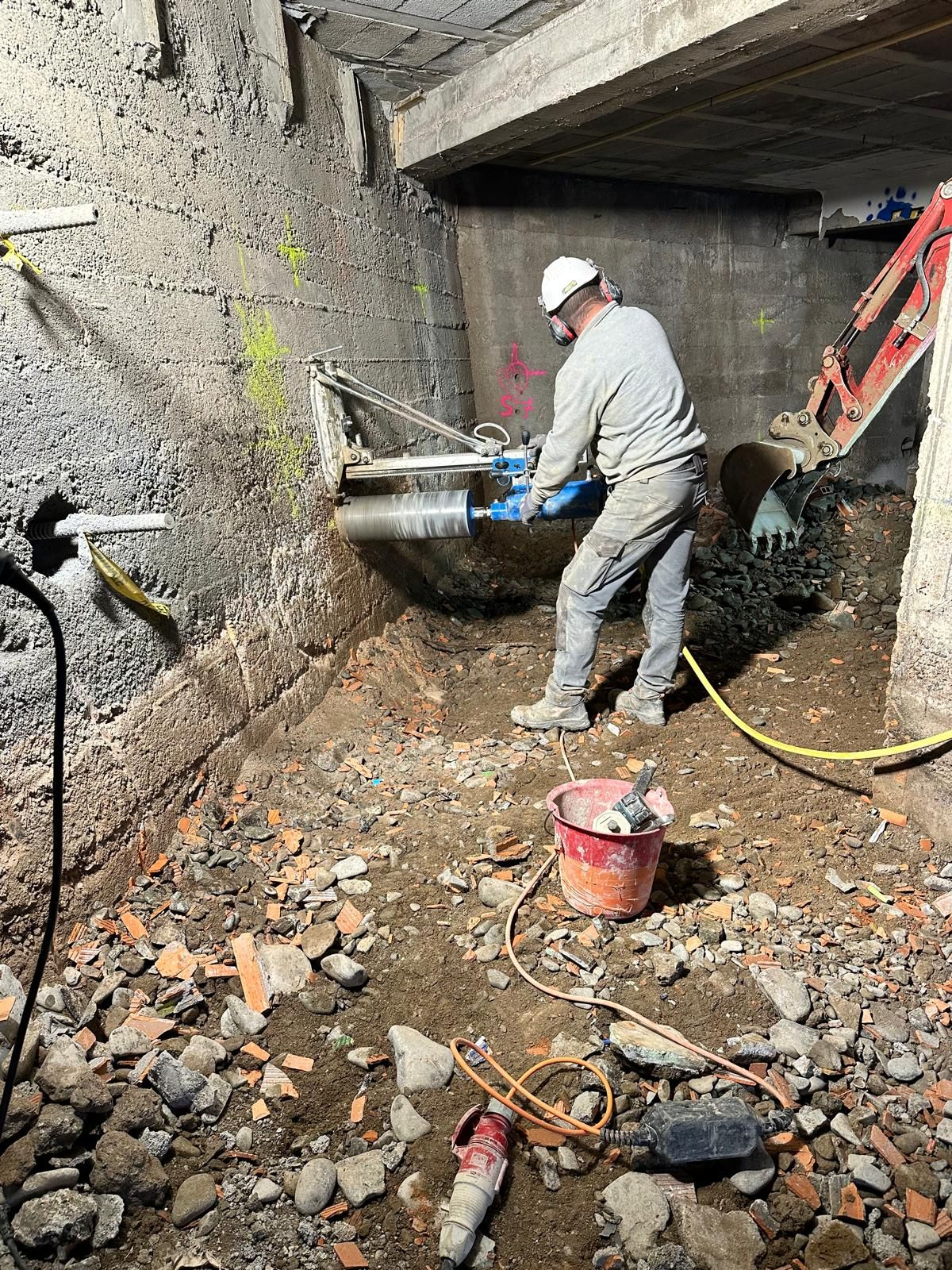 Une grande scie circulaire coupe un mur de béton dans un environnement de construction, avec des rochers à la base.