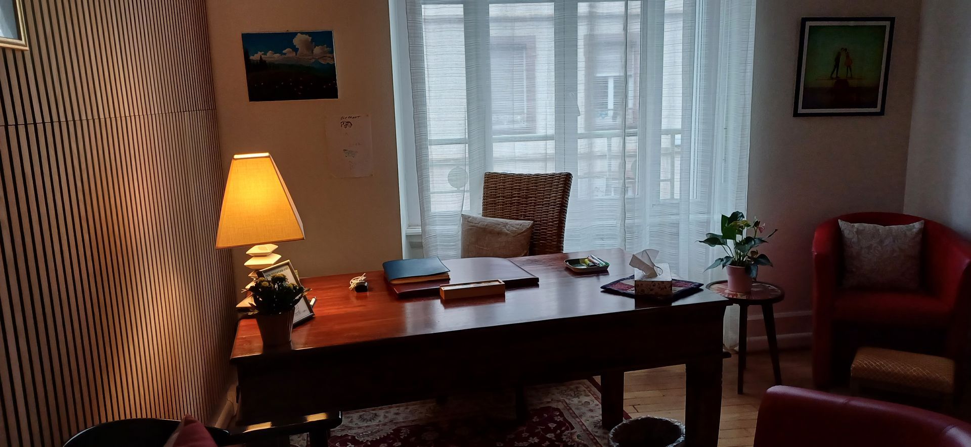 Bureau cosy avec un bureau, une chaise, un fauteuil et une fenêtre. Éclairage chaleureux et papier peint à motifs.