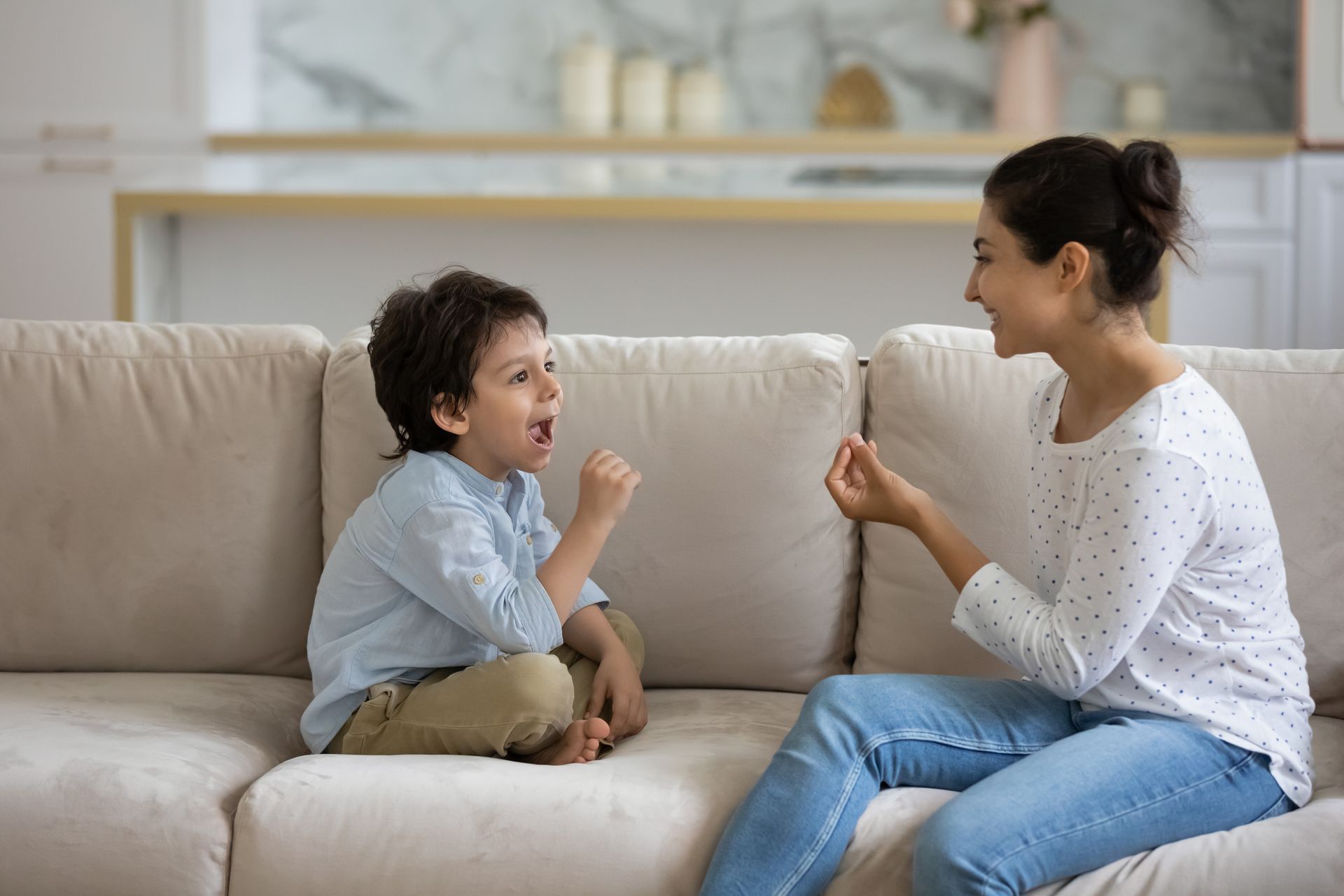 Une femme et un enfant sont assis sur un canapé et s'exercent à communiquer. L'enfant gesticule et parle.