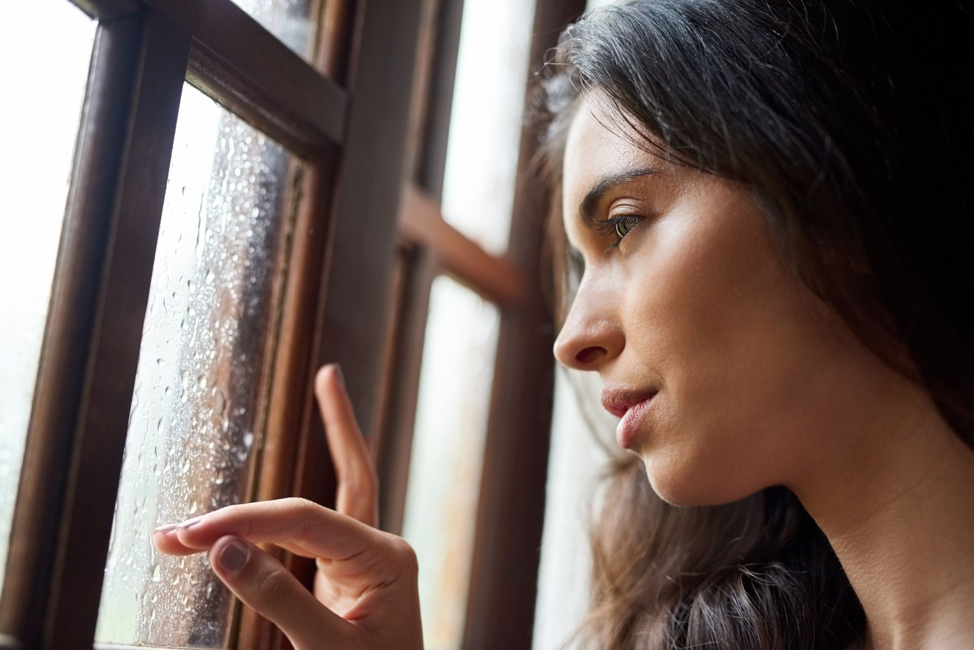Une femme regarde la pluie par la fenêtre en touchant la vitre. Cadre de fenêtre.