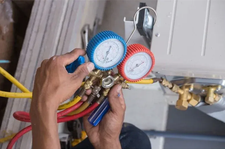 Manos conectando medidores a una unidad de aire acondicionado, utilizando mangueras amarillas, rojas y azules.