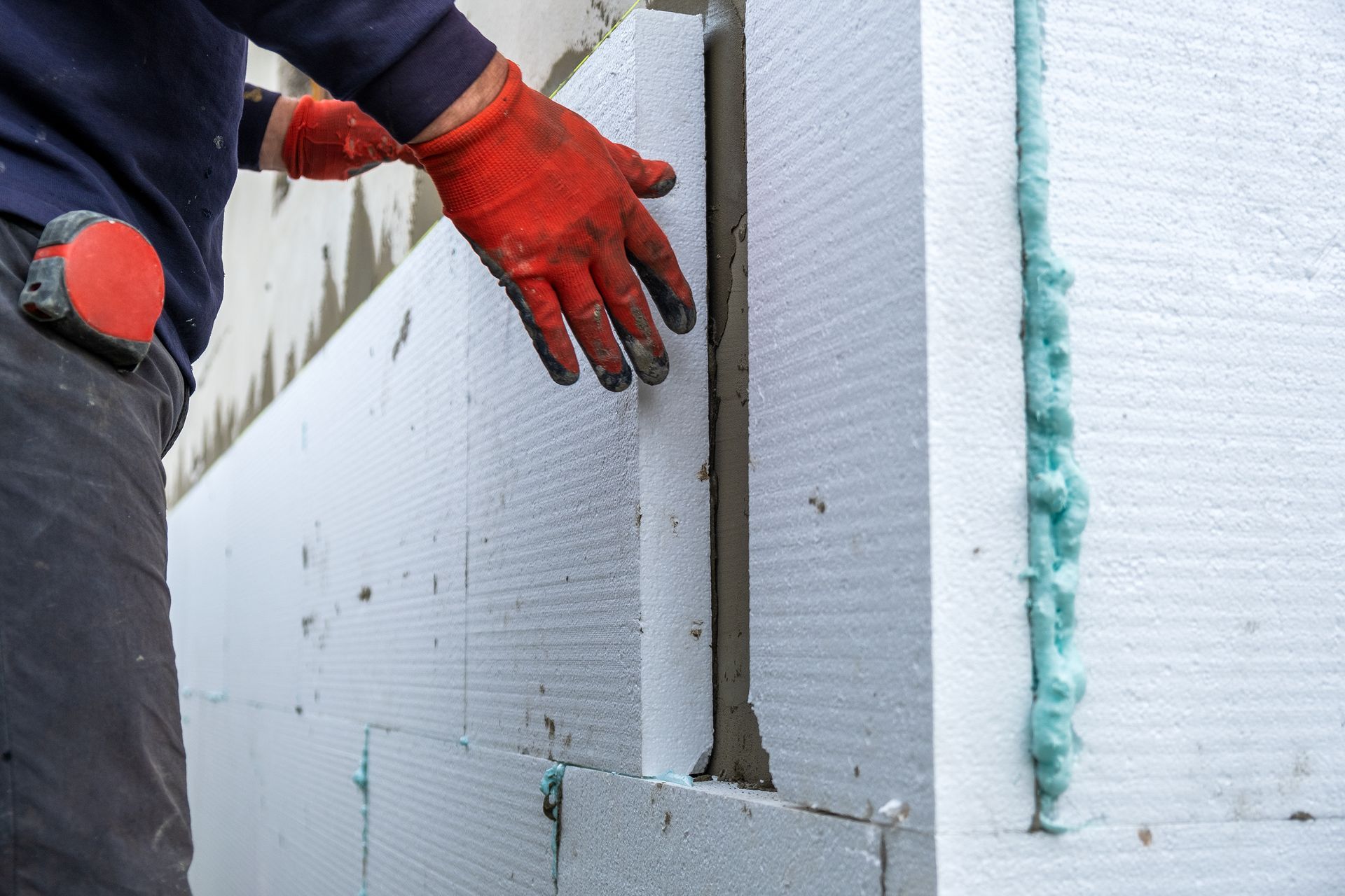 Un ouvrier du bâtiment installe des feuilles d'isolation en polystyrène sur le mur de la façade d'une maison pour la protection thermique